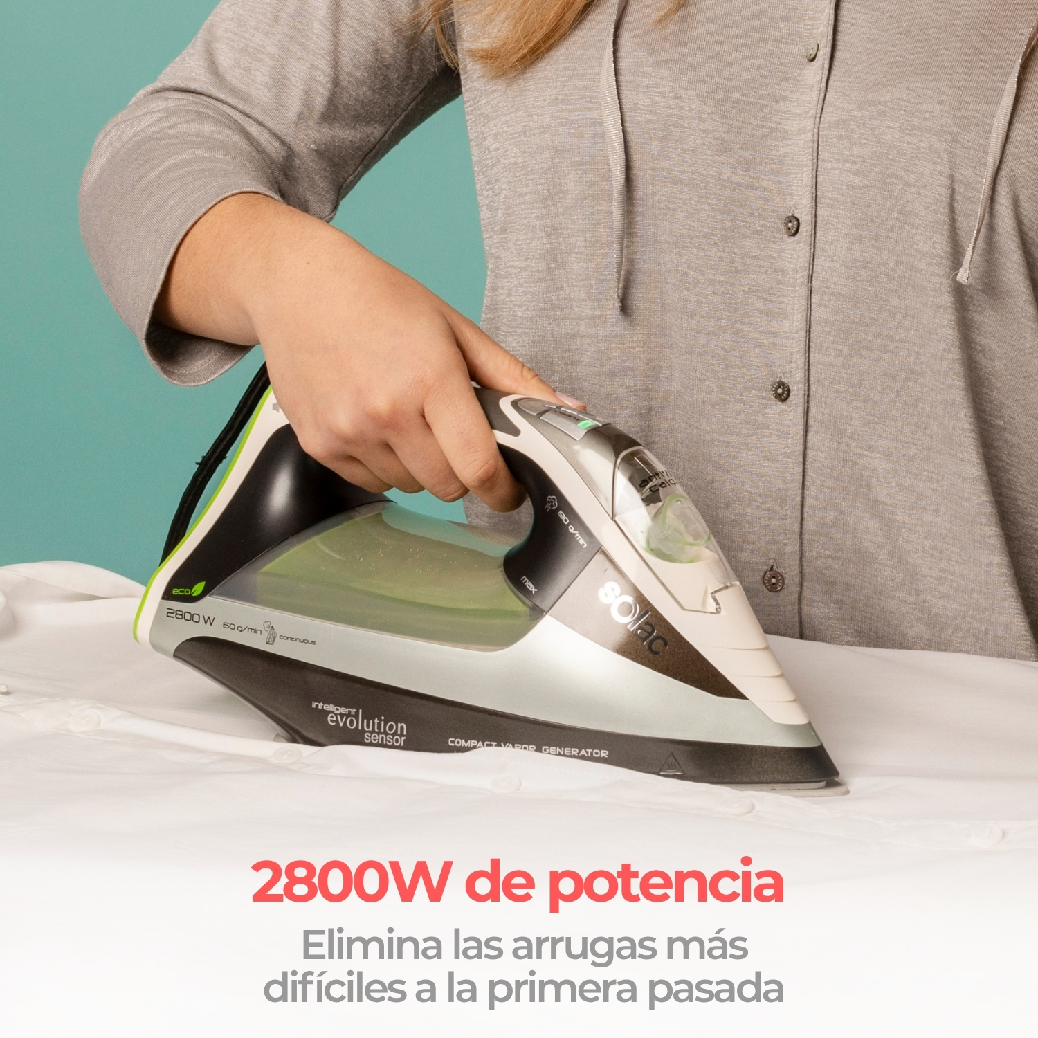 Una mano plancha una camisa blanca con una moderna plancha de vapor negra y gris sobre fondo turquesa.
