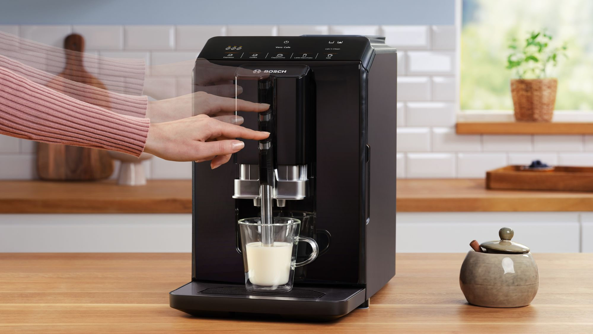 Una mano ajusta la altura del surtidor de café en una cafetera Bosch negra en una cocina.