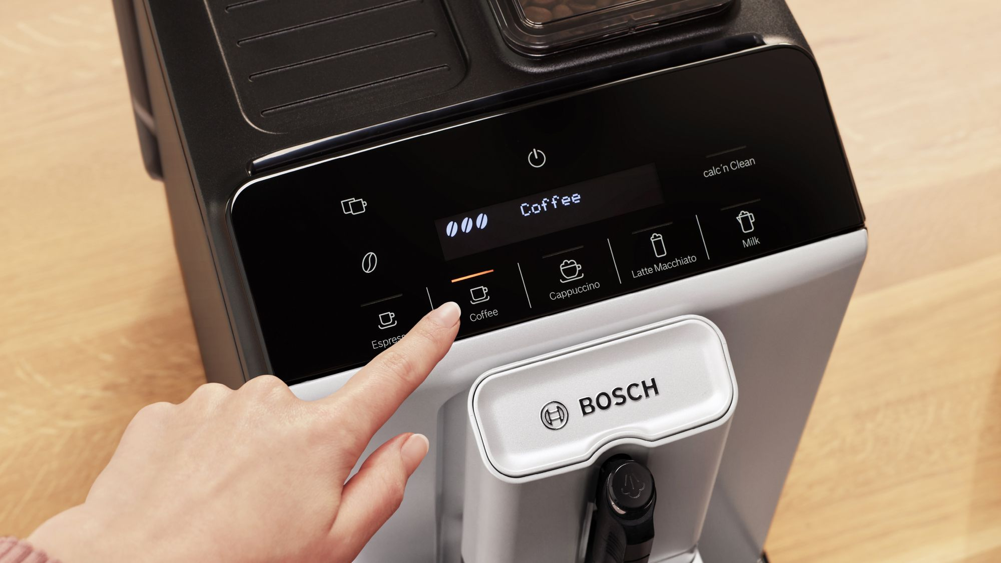Un dito tocca il display touch di una macchina da caffè Bosch con la scritta Coffee.