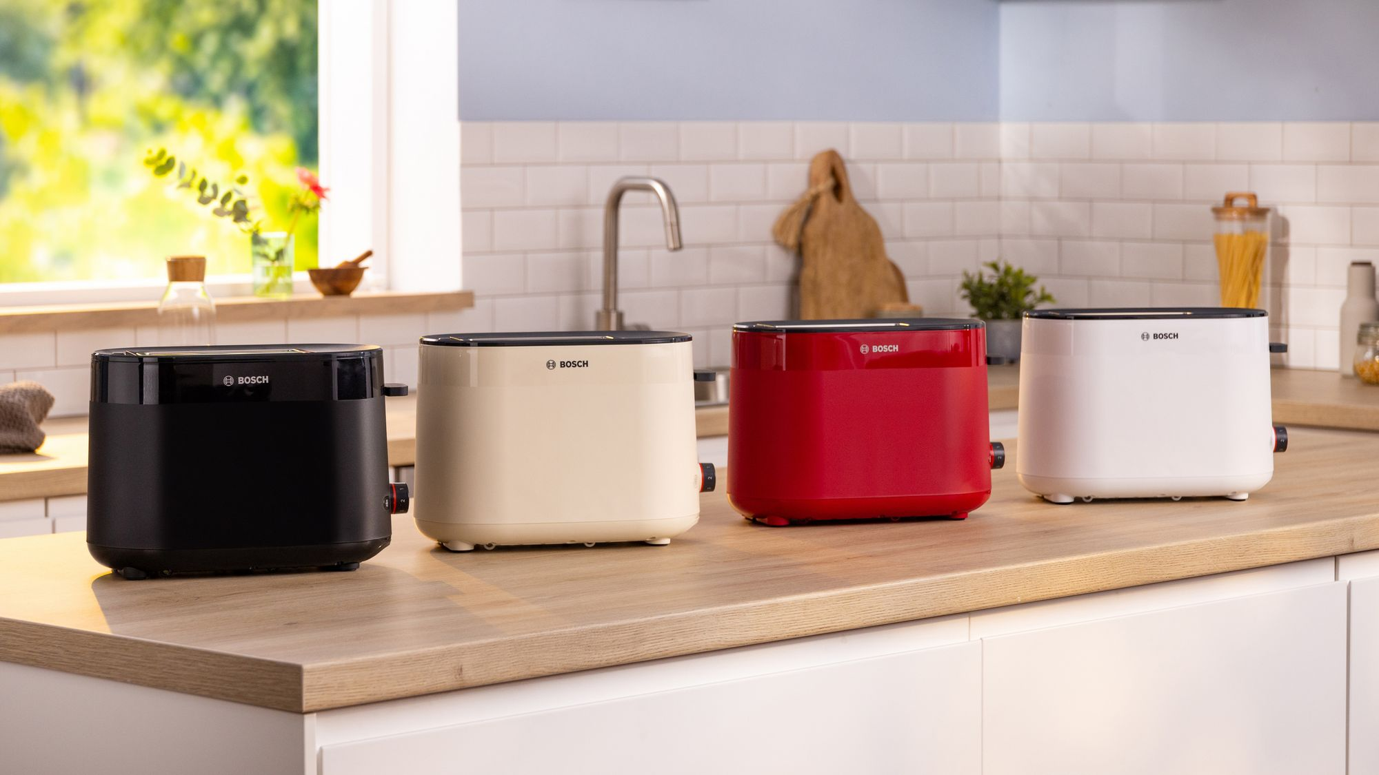 Cuatro tostadoras Bosch en negro, beige, rojo y blanco se encuentran en una encimera de madera en una cocina luminosa.