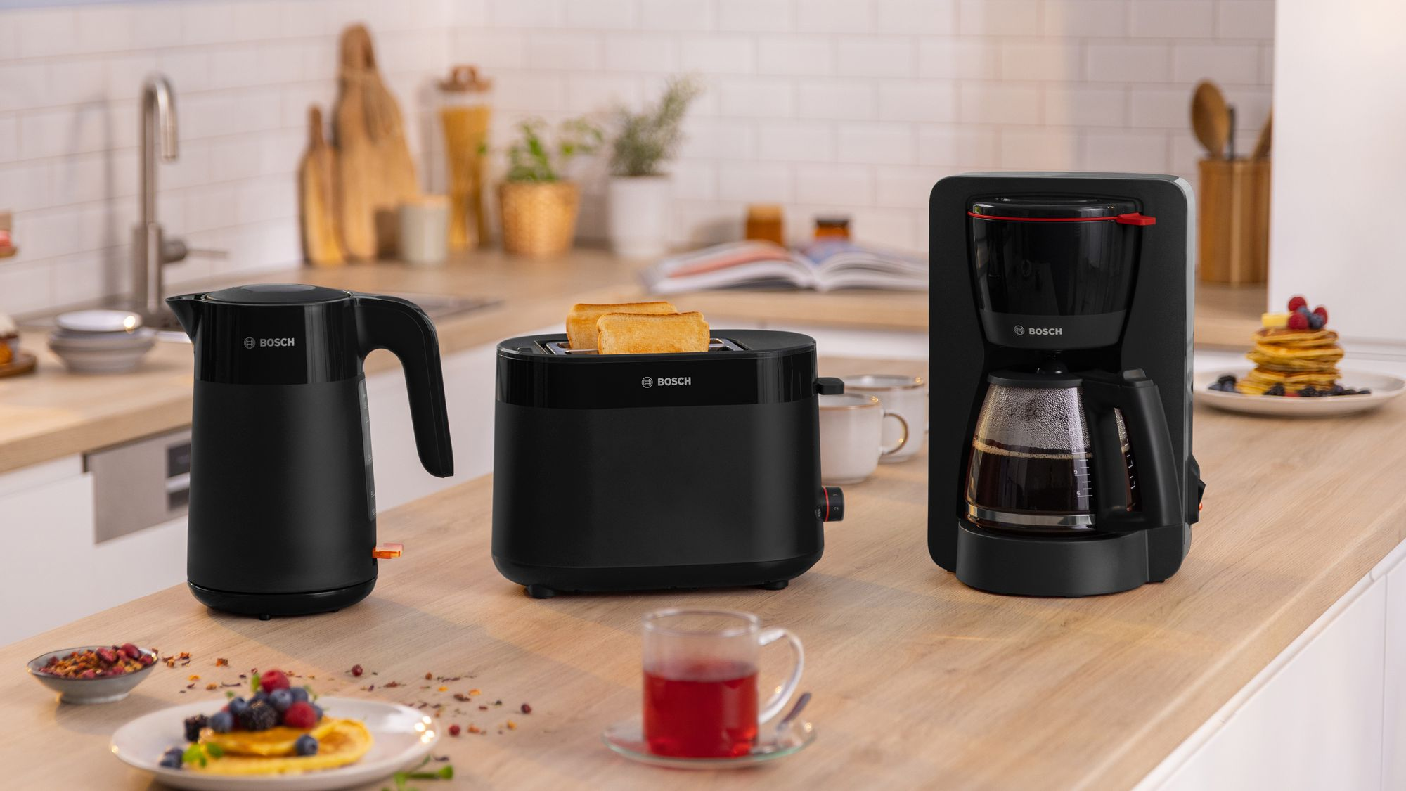Electrodomésticos negros Bosch, incluidos hervidor, tostadora y cafetera, sobre una encimera de madera en una cocina.