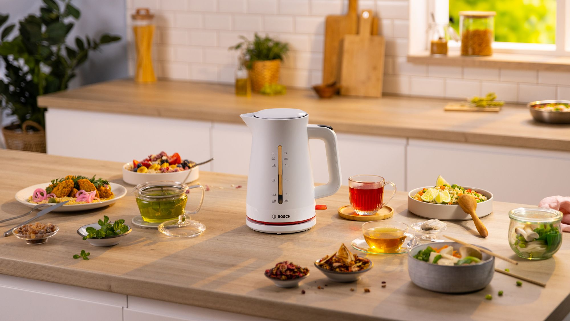 Un hervidor eléctrico Bosch blanco sobre una encimera de madera rodeado de cuencos de comida, té e ingredientes.