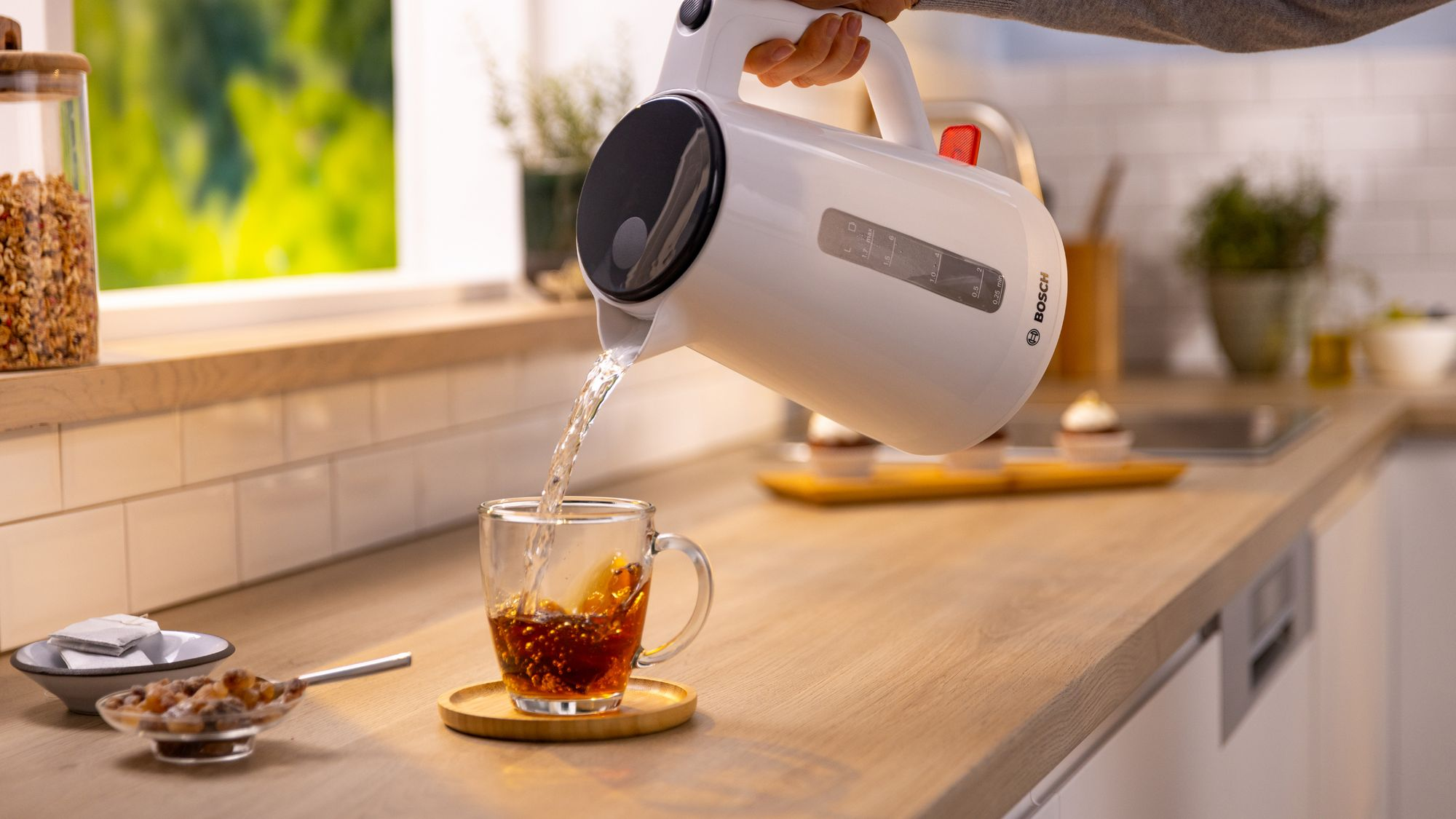 Un hervidor blanco Bosch vierte agua caliente en una taza de té en un mostrador de madera en una cocina.