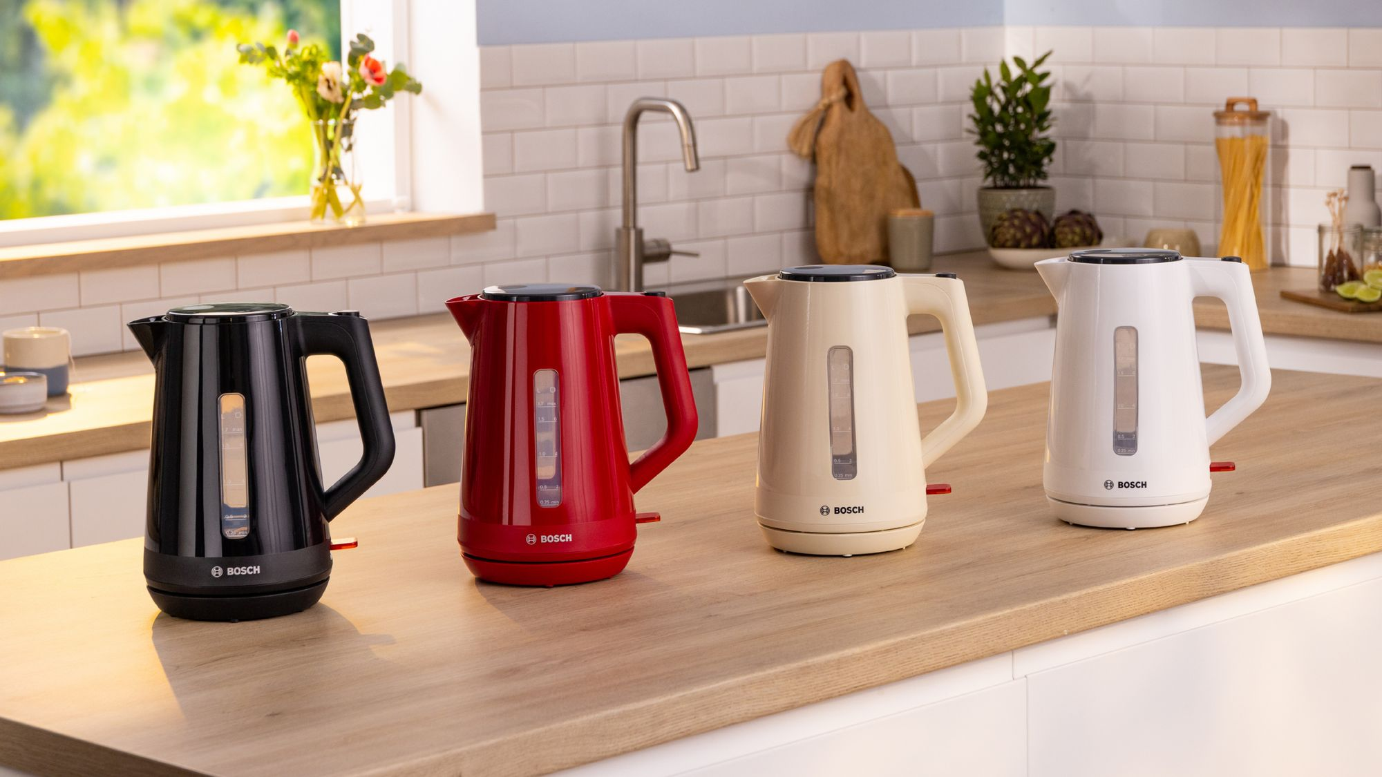 Cuatro hervidores Bosch en negro, rojo, beis y blanco sobre una encimera de madera en una cocina moderna.
