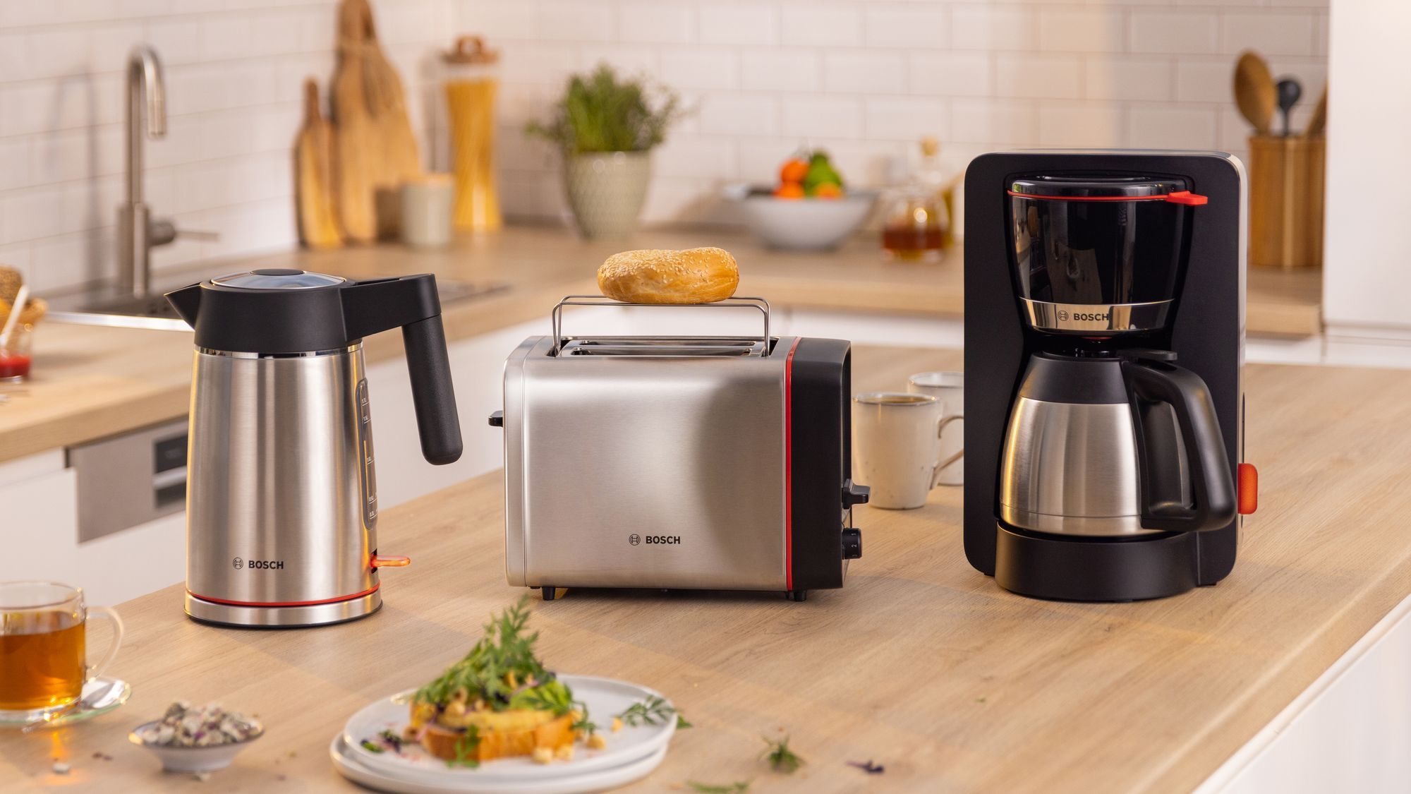 Un piano cucina con bollitore in acciaio inossidabile, tostapane con bagel e una macchina da caffè nera.