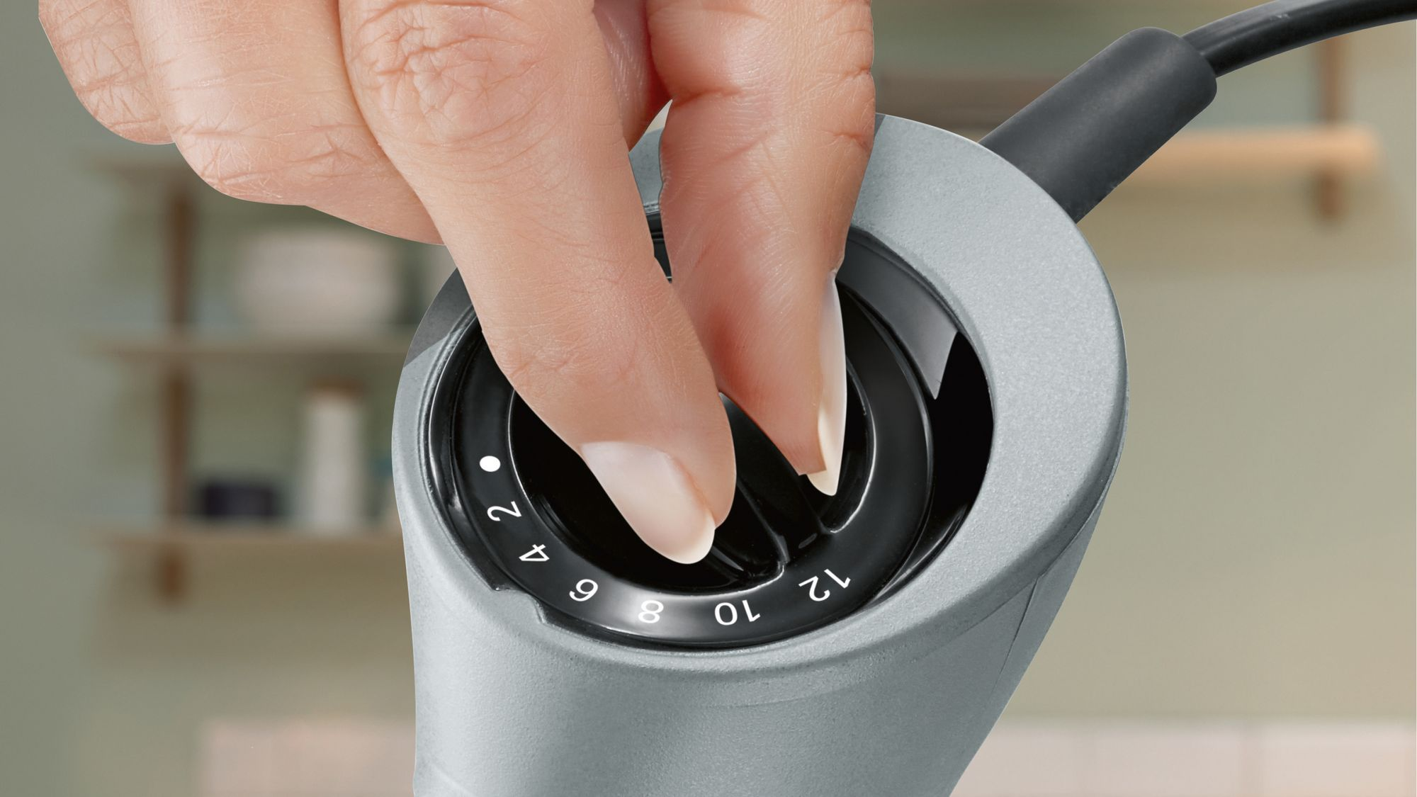 Una mano ajusta el selector de velocidad de un electrodoméstico gris, numerado del dos al doce.