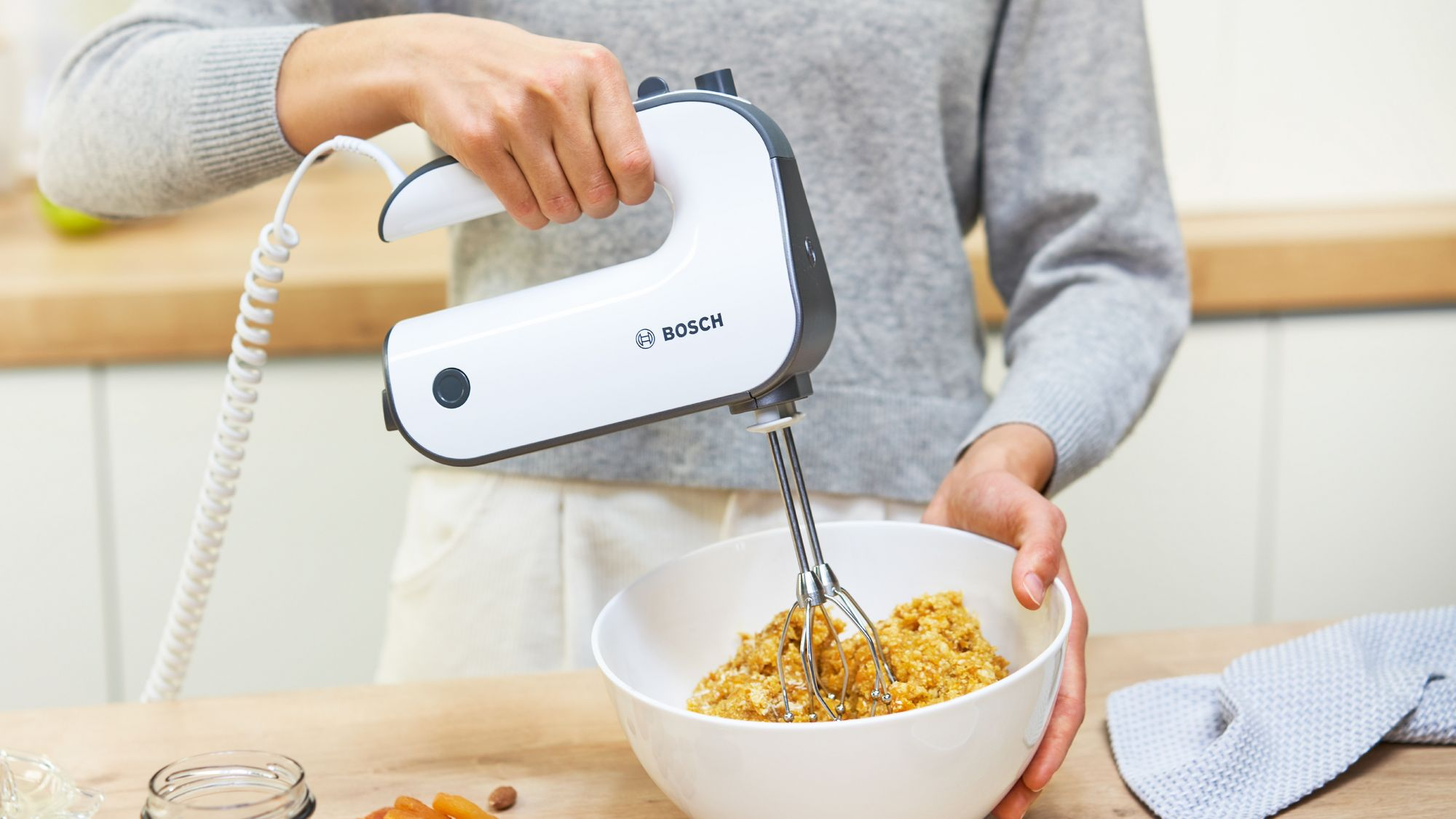 Person mixt Teig in einer weißen Schüssel mit einem weißen Bosch Handrührgerät.