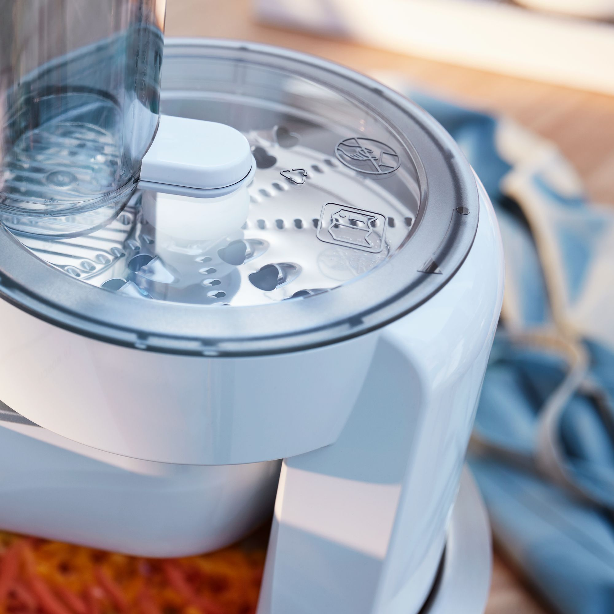Un electrodoméstico blanco con tapa transparente y rallador metálico, con zanahorias ralladas.