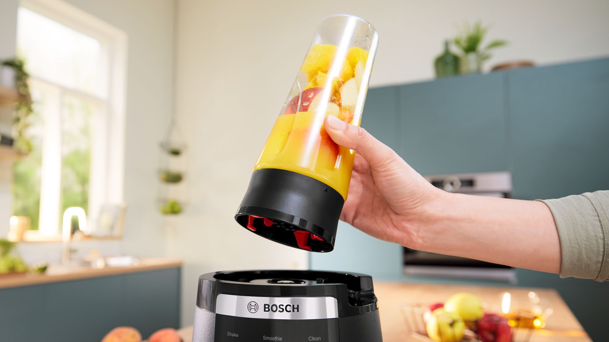 Aydinlik bir mutfakta bir el, dolu blender haznesini Bosch blender tabani üzerine tutuyor.