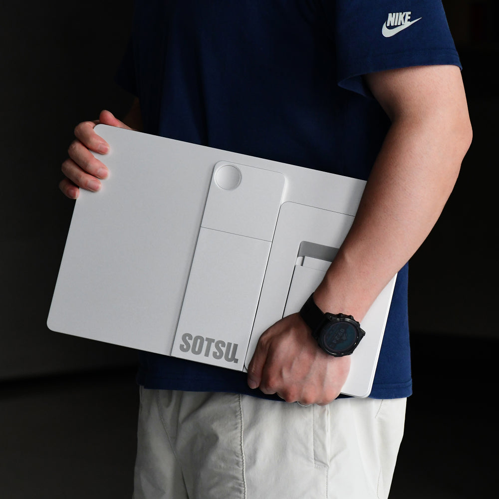 Osoba w niebieskiej koszulce Nike i zegarku trzyma białą składaną tablicę SOTSU.