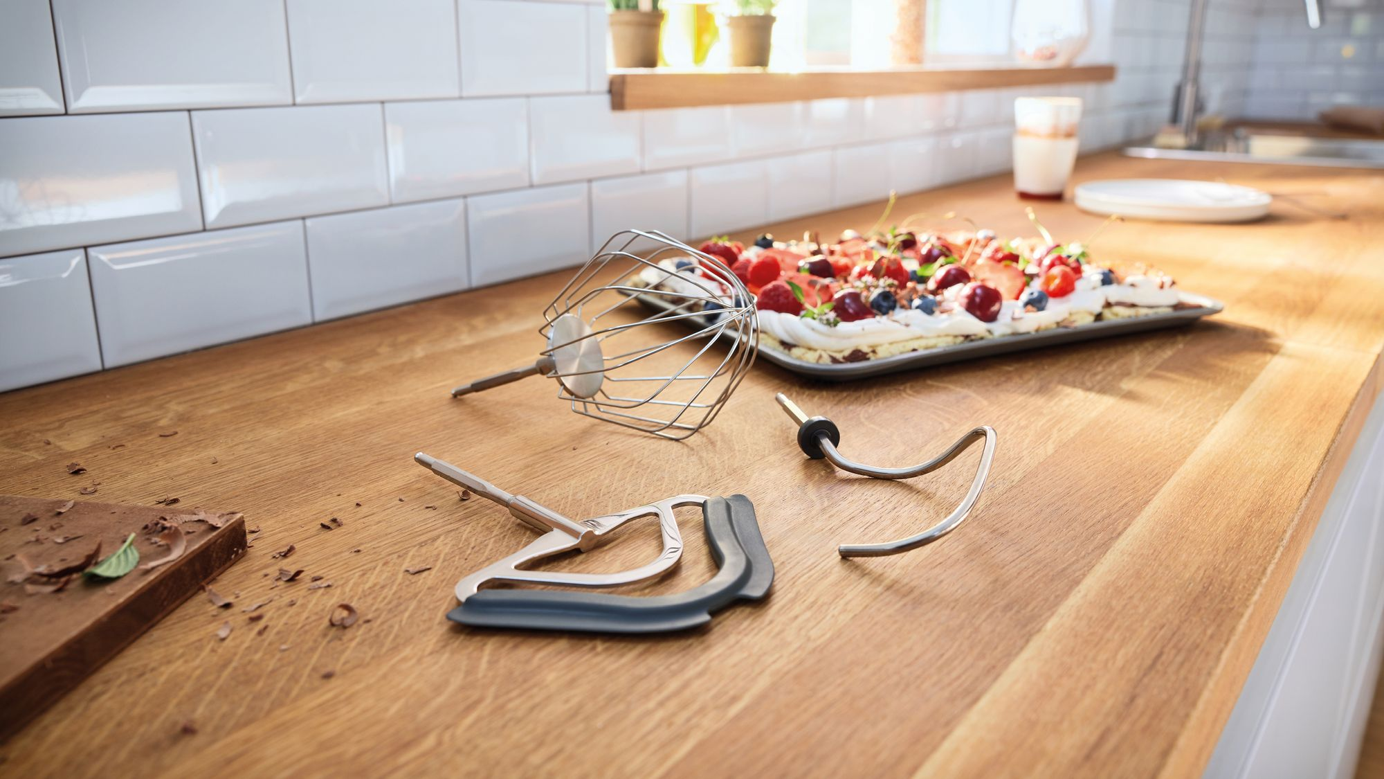 Accessori per frusta su un bancone da cucina in legno con una torta ai frutti di bosco.
