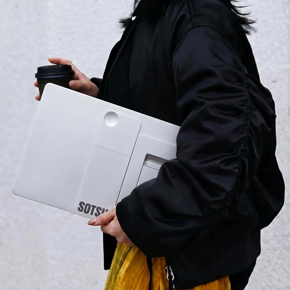 Una mujer con chaqueta negra sostiene una laptop blanca y un vaso de café.