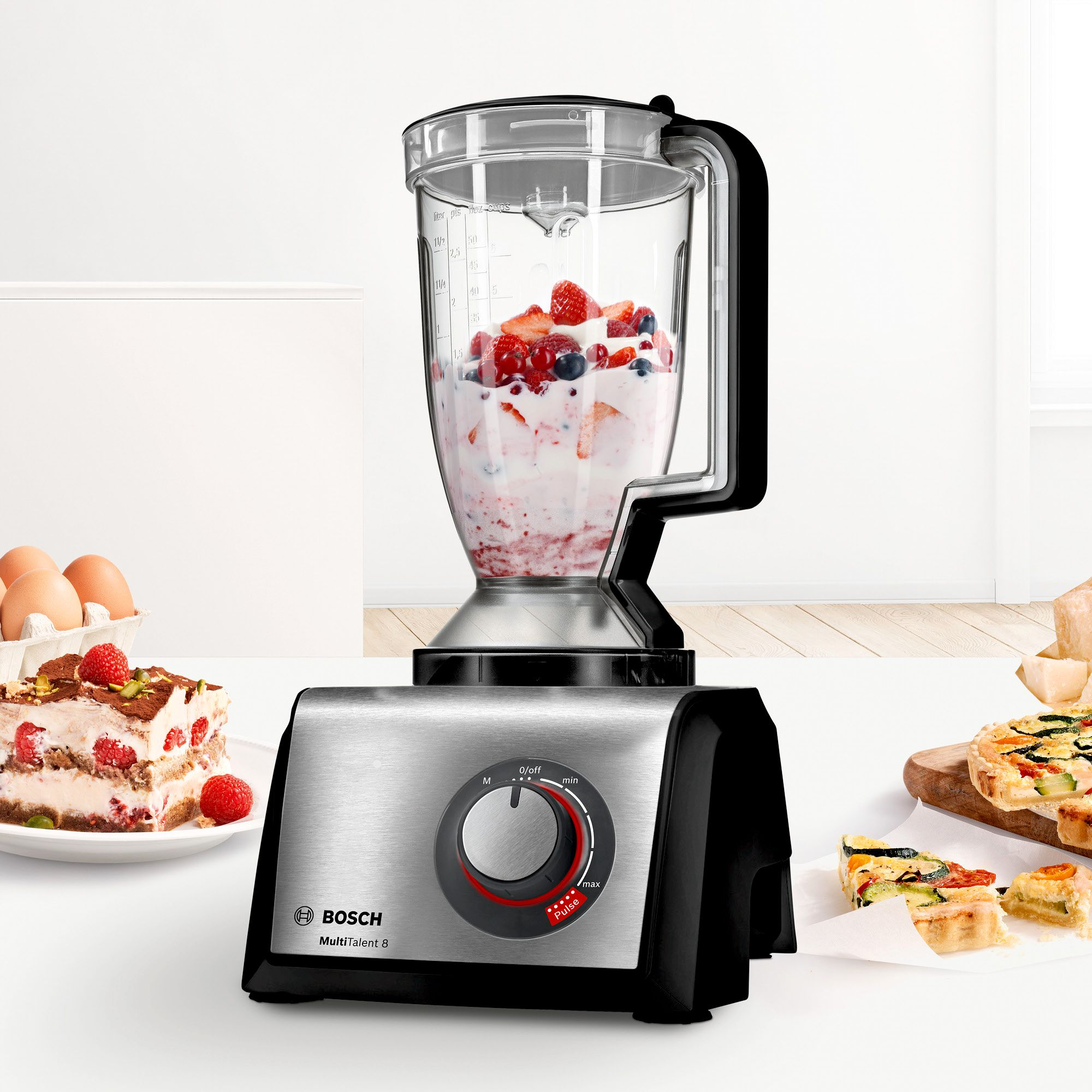 Una licuadora Bosch MultiTalent 8 con leche y bayas en una mesa, rodeada de tarta y quiche.