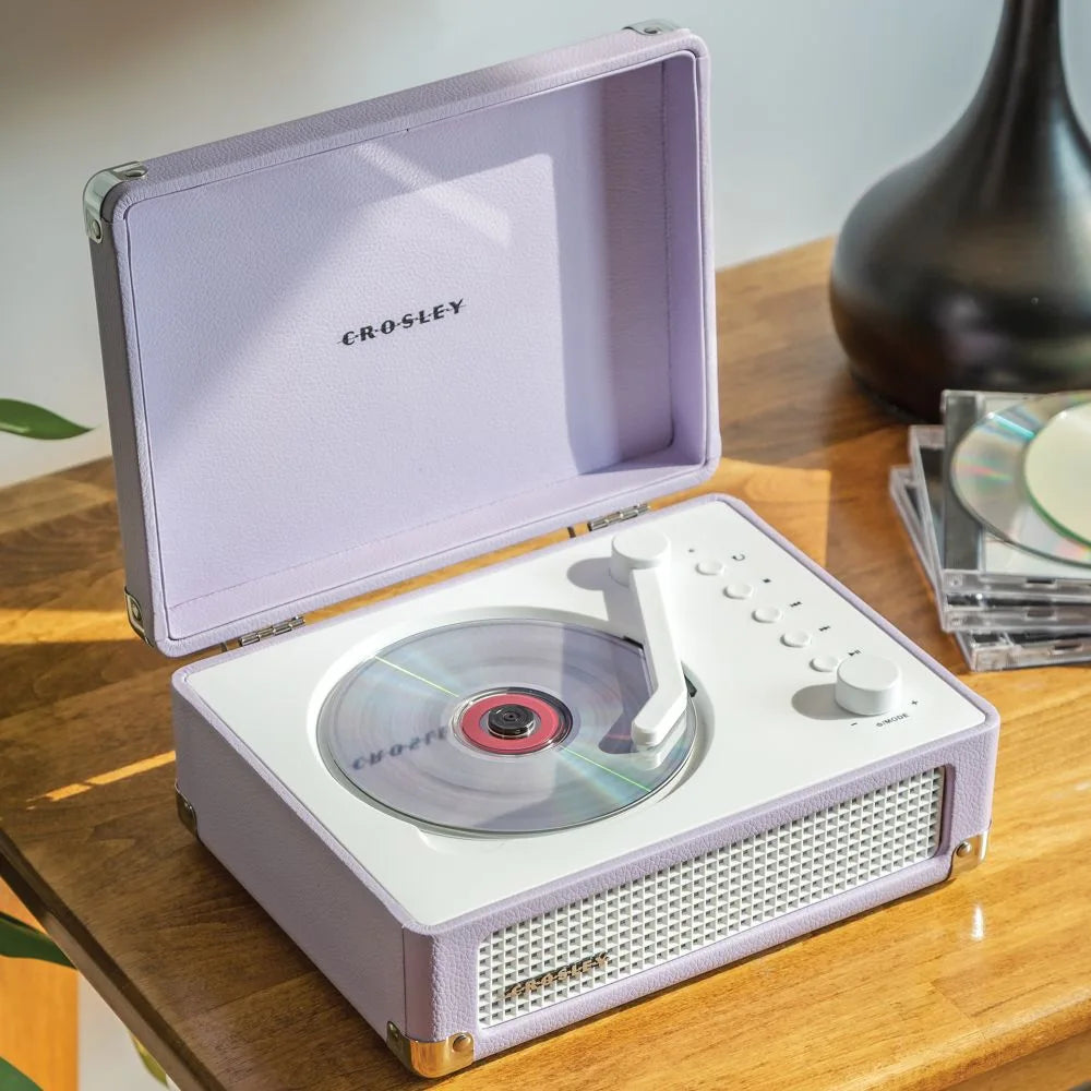 Ein offener lavendelfarbener Koffer-Plattenspieler mit einer CD im Inneren steht auf einem Holztisch.