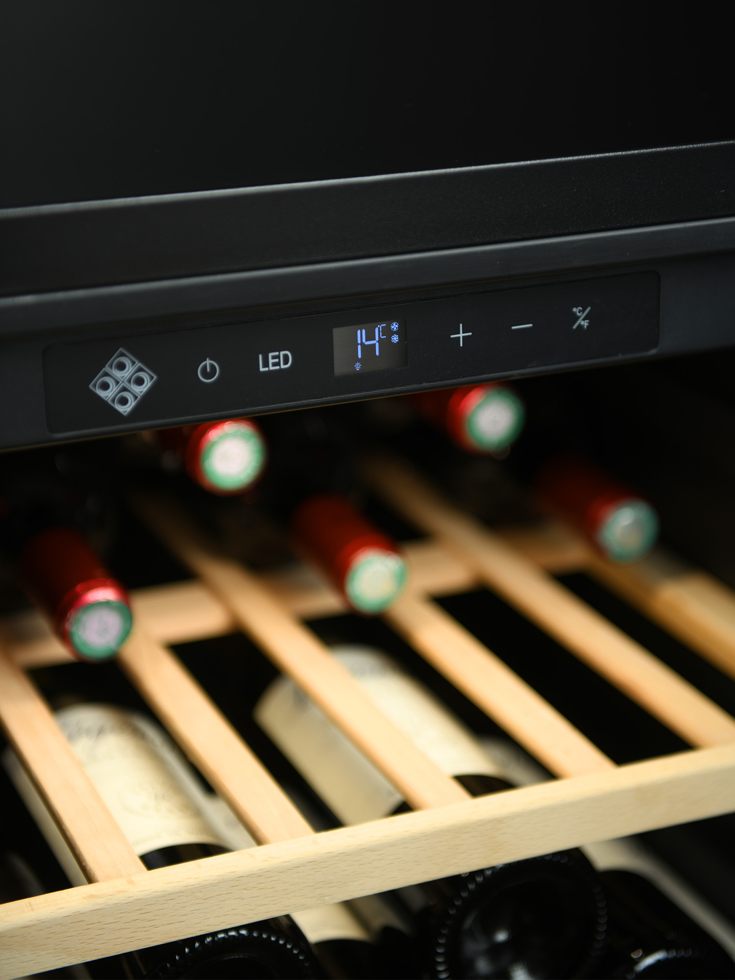 Vinoteca con pantalla digital a 14 grados, estantes de madera y botellas almacenadas.