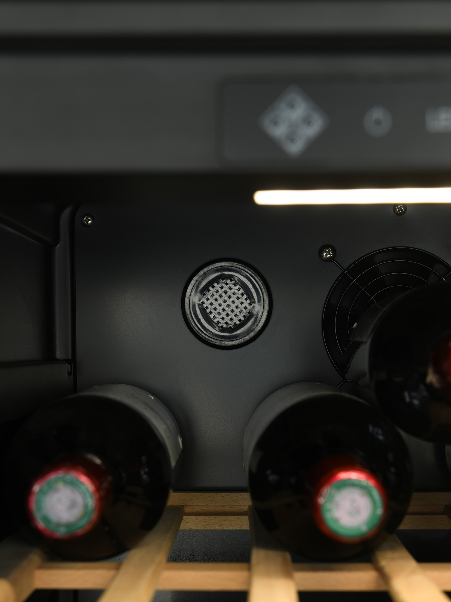 Interior de vinoteca con estantes de madera y botellas de vino tinto. Un ventilador circular está en el fondo.
