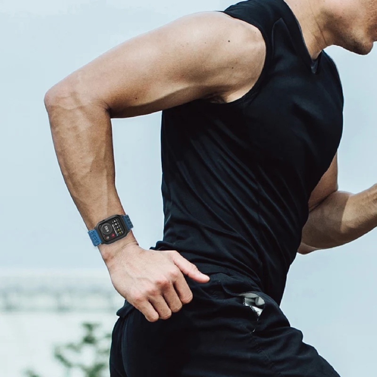 Ein Sportler in schwarzer Kleidung läuft draußen und trägt eine Smartwatch mit blauem Armband.
