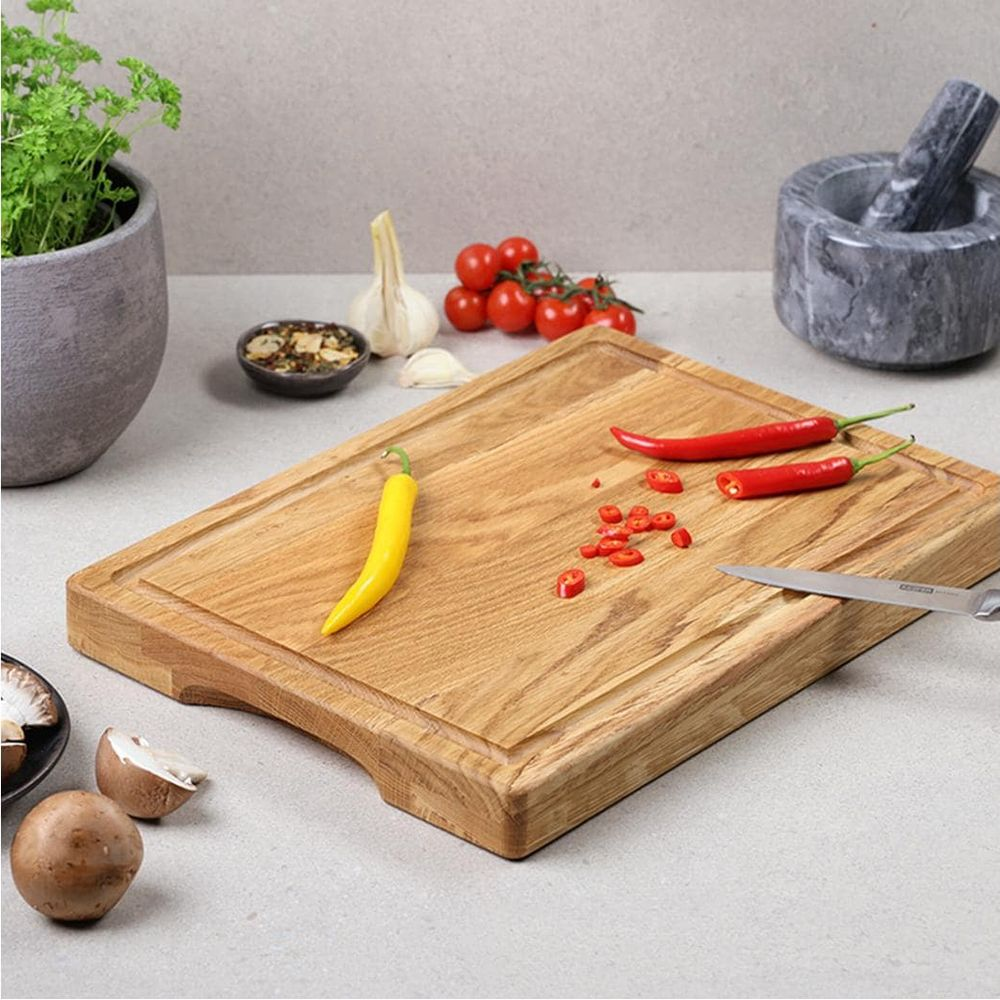 Ein Holzschneidebrett mit roten und gelben Chilis, Tomaten, Kräutern und Pilzen auf der Arbeitsplatte.