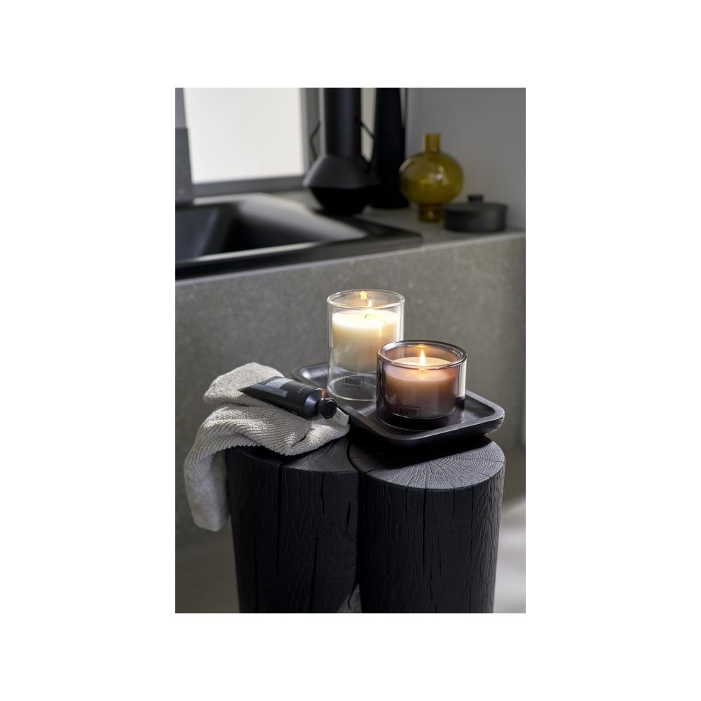 Candele profumate e un asciugamano grigio su uno sgabello di legno nero in bagno.