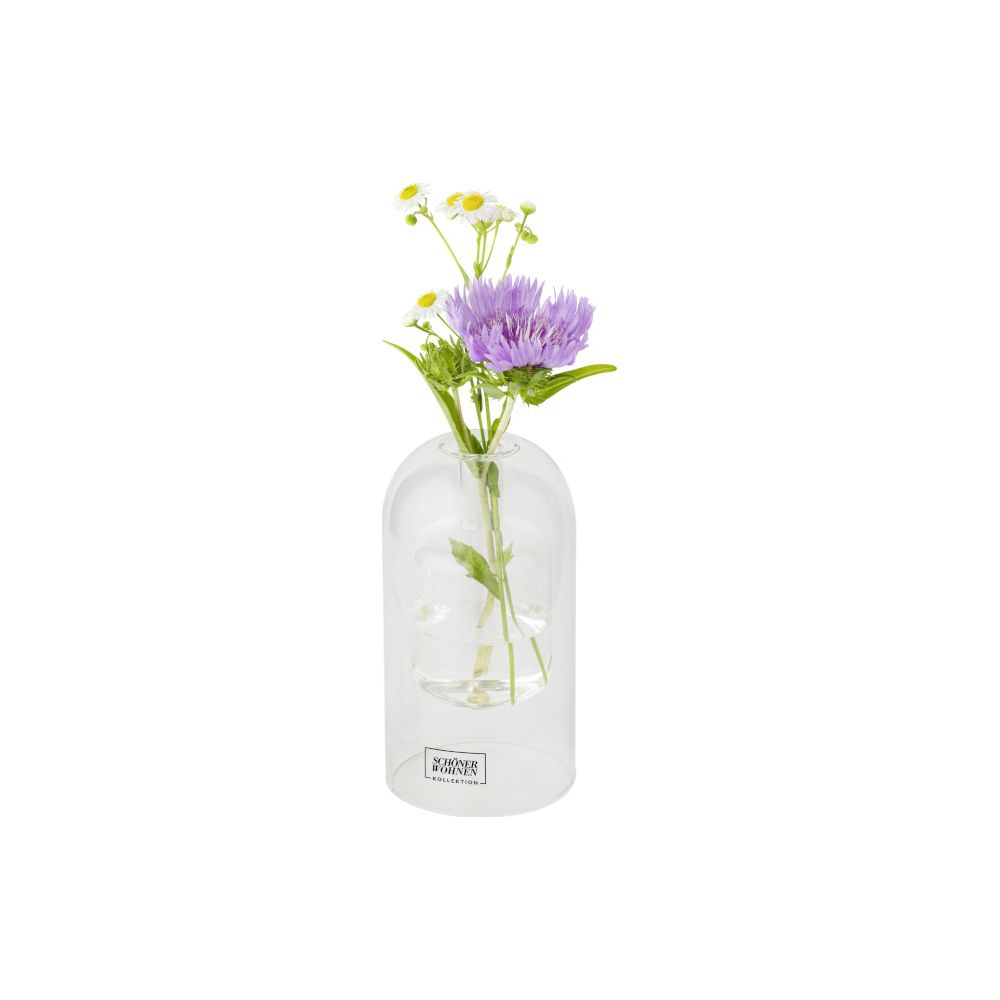 Un vaso di vetro trasparente con piccole margherite bianche e un grande fiore viola su sfondo bianco.
