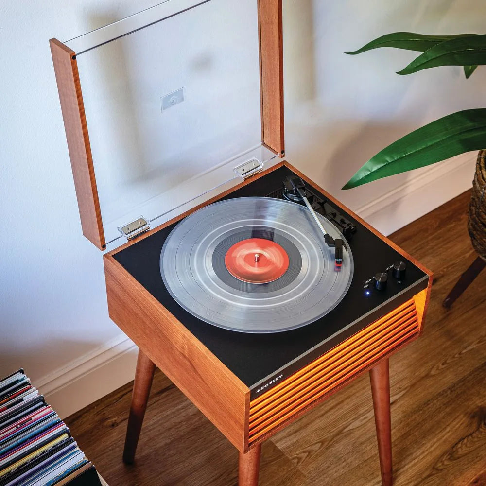 Ein Holzdrehteller mit einer klaren Schallplatte spielt Musik, neben einem Stapel Platten und einer Pflanze.