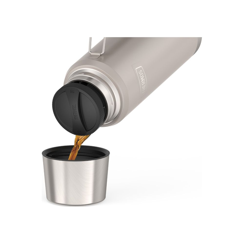 Eine graue Thermoskanne gießt Kaffee in einen silbernen Becher vor weißem Hintergrund.