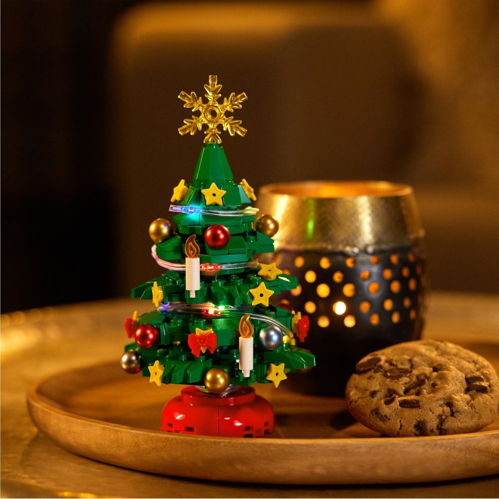 Ein Spielzeug-Weihnachtsbaum aus grünen Steinen auf einem Tablett mit Kerze und Keks.