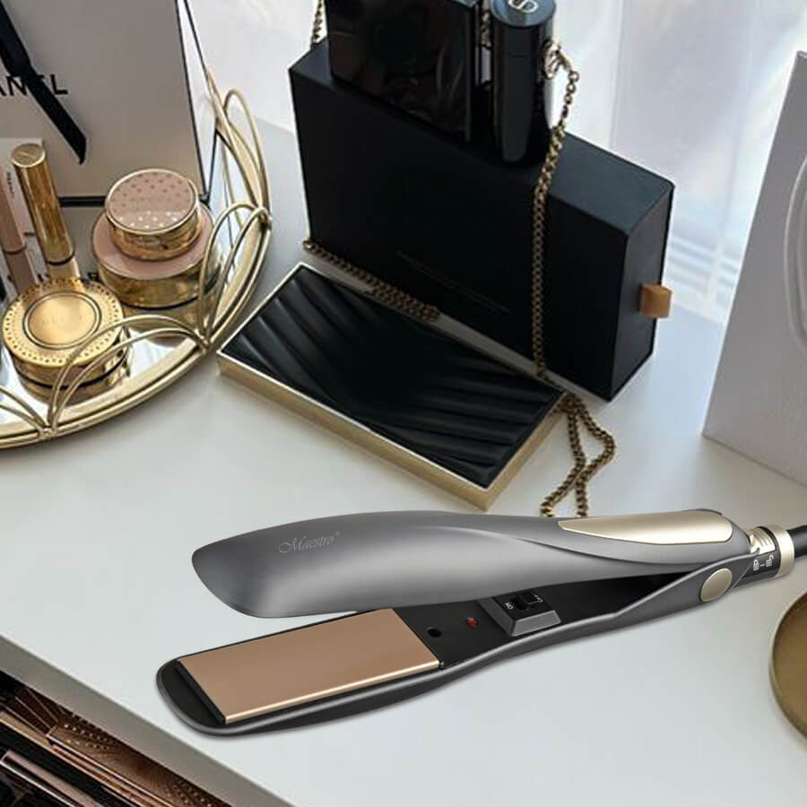 Una piastra per capelli grigia e oro su un tavolo bianco con cosmetici e scatole regalo.