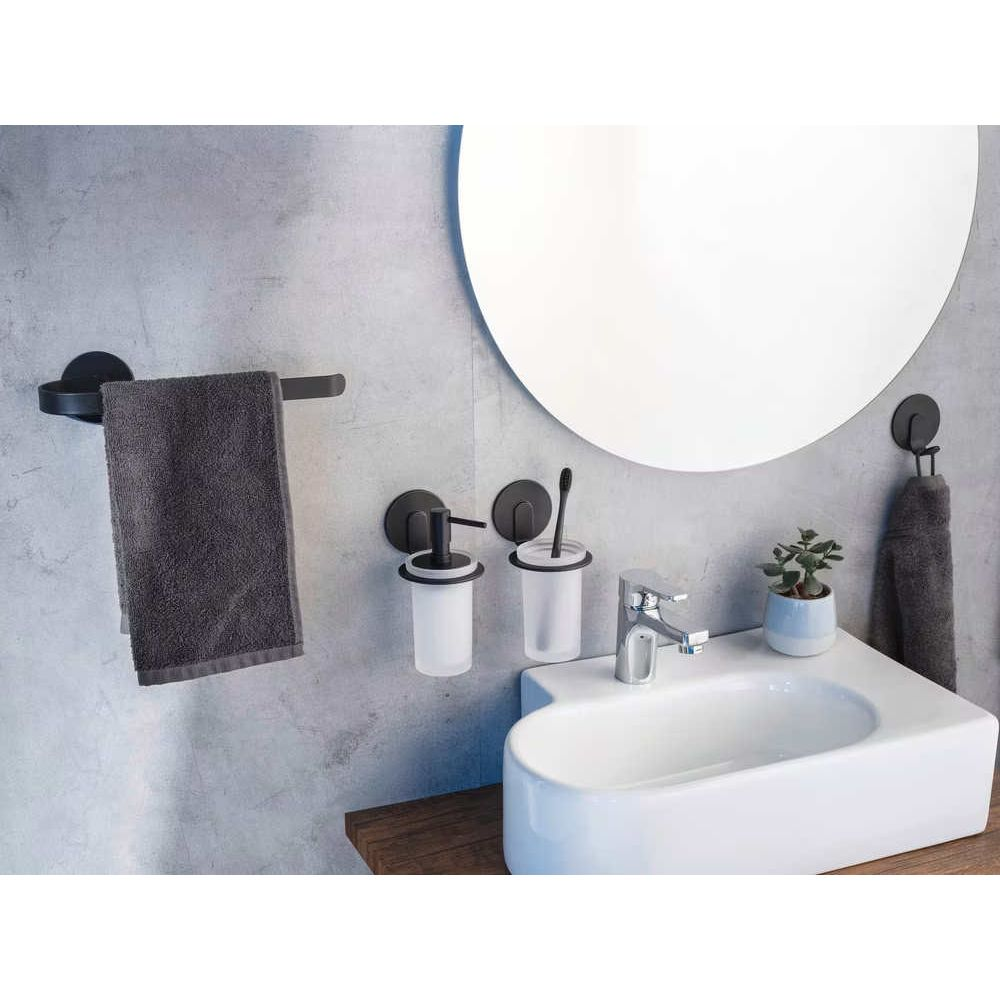 Ein modernes Badezimmer mit grauen Accessoires, schwarzem Handtuchhalter, Waschbecken und rundem Spiegel vor Betonwand.