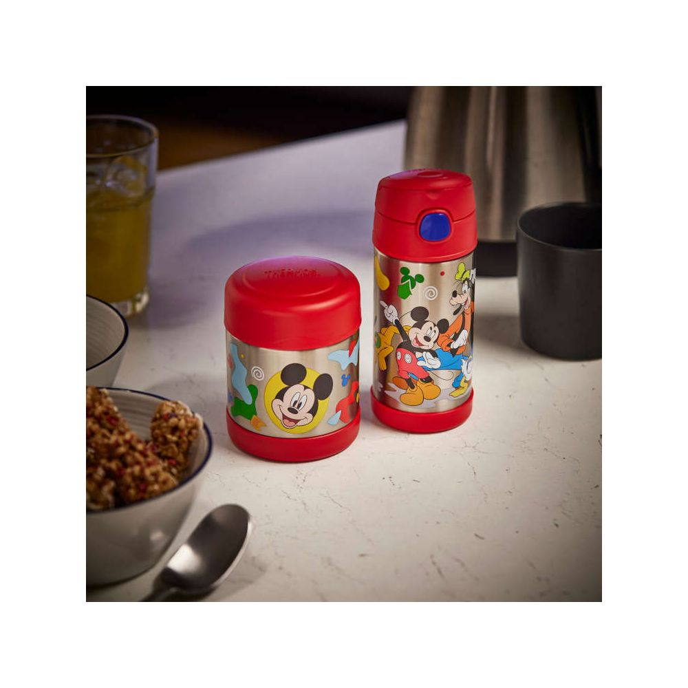 Zwei farbige Thermosbehälter mit Micky-Maus-Motiven stehen auf einer weißen Küchentheke mit Geschirr.