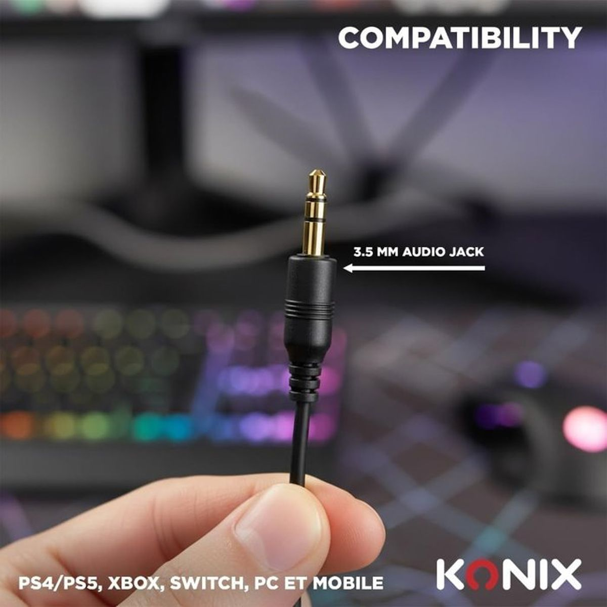 Una mano tiene un jack audio da 3,5 mm su sfondo sfocato con tastiera RGB.
