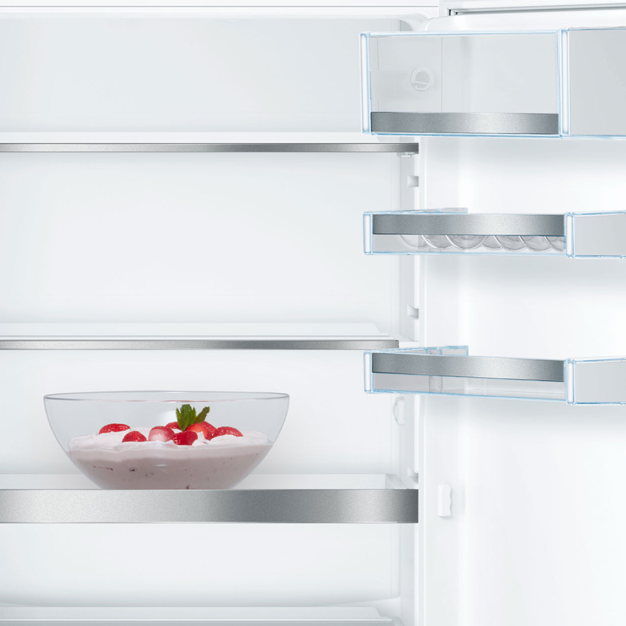 Un frigorifero bianco aperto con una ciotola di vetro di crema alle fragole sul ripiano inferiore.
