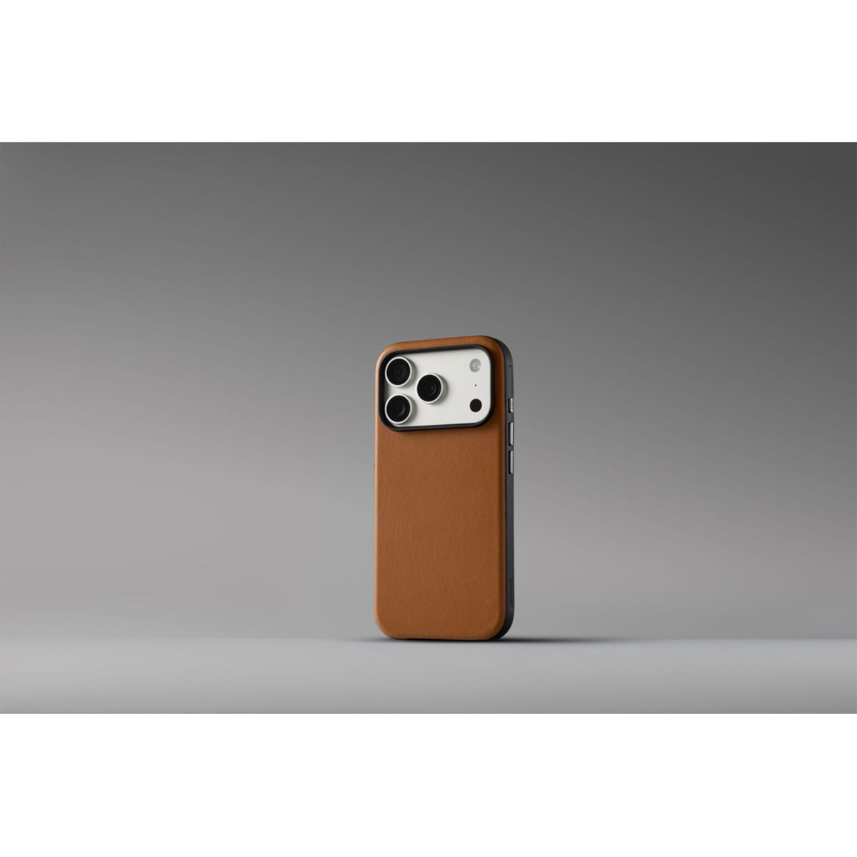 Uno smartphone in custodia di pelle marrone si erge verticalmente su superficie grigia con sfondo minimalista.