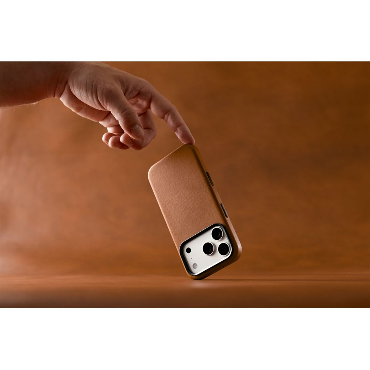 Eine Hand tippt auf ein Smartphone in einer braunen Lederhülle vor braunem Hintergrund.