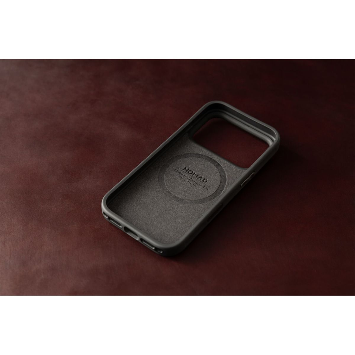 Eine graue Smartphone-Hülle liegt auf einem dunkelroten Ledertisch.