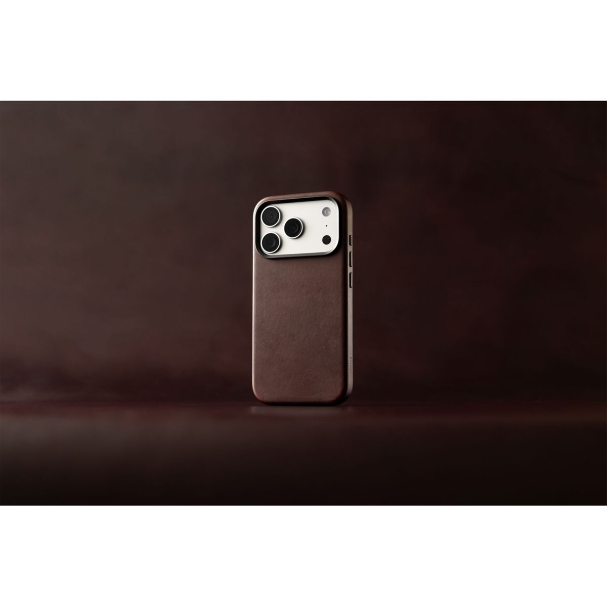 Ein Smartphone in einer braunen Lederhülle steht aufrecht auf einer passenden braunen Oberfläche vor dunklem Hintergrund.