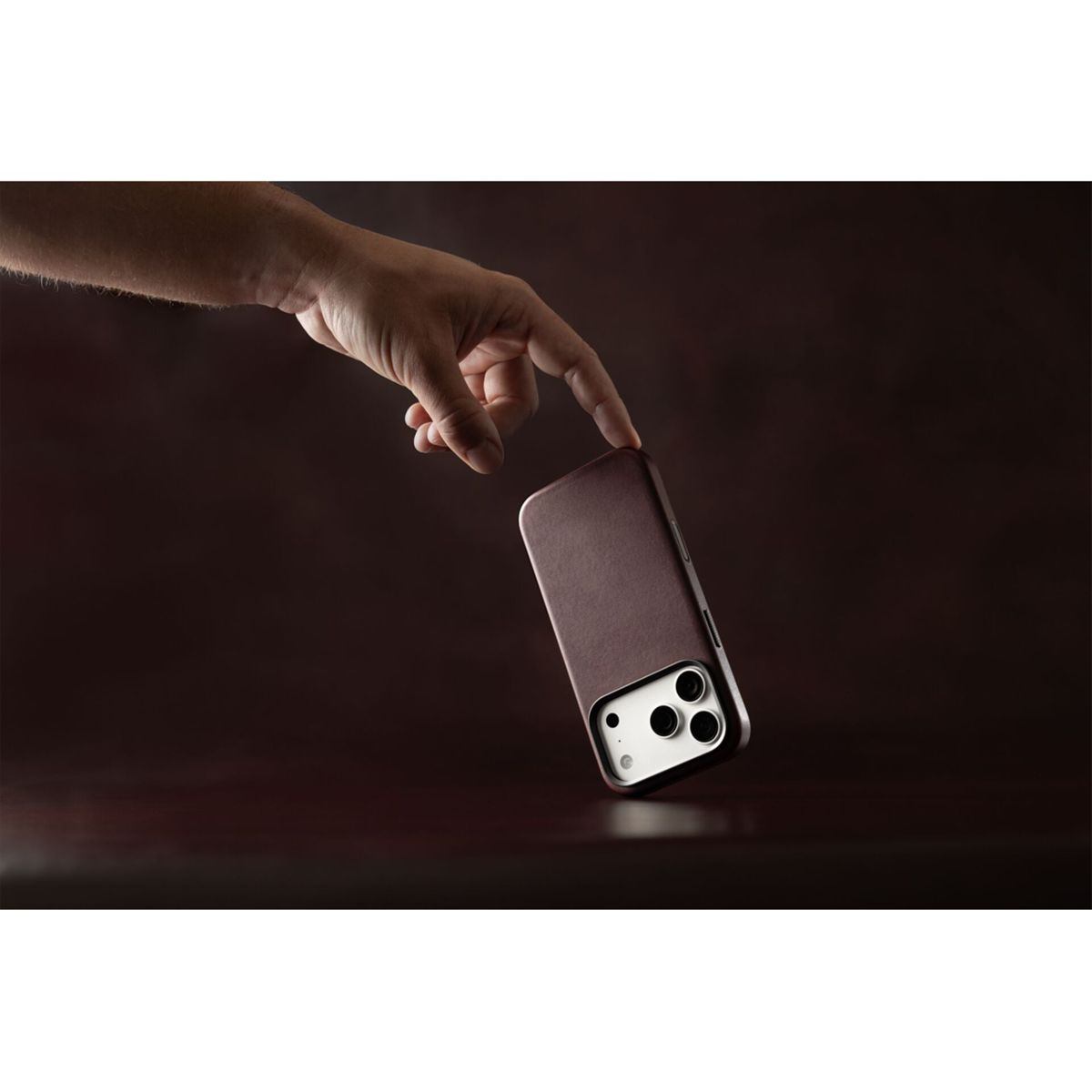 Eine Hand zeigt auf ein Smartphone in einer braunen Lederhülle vor dunklem Hintergrund.