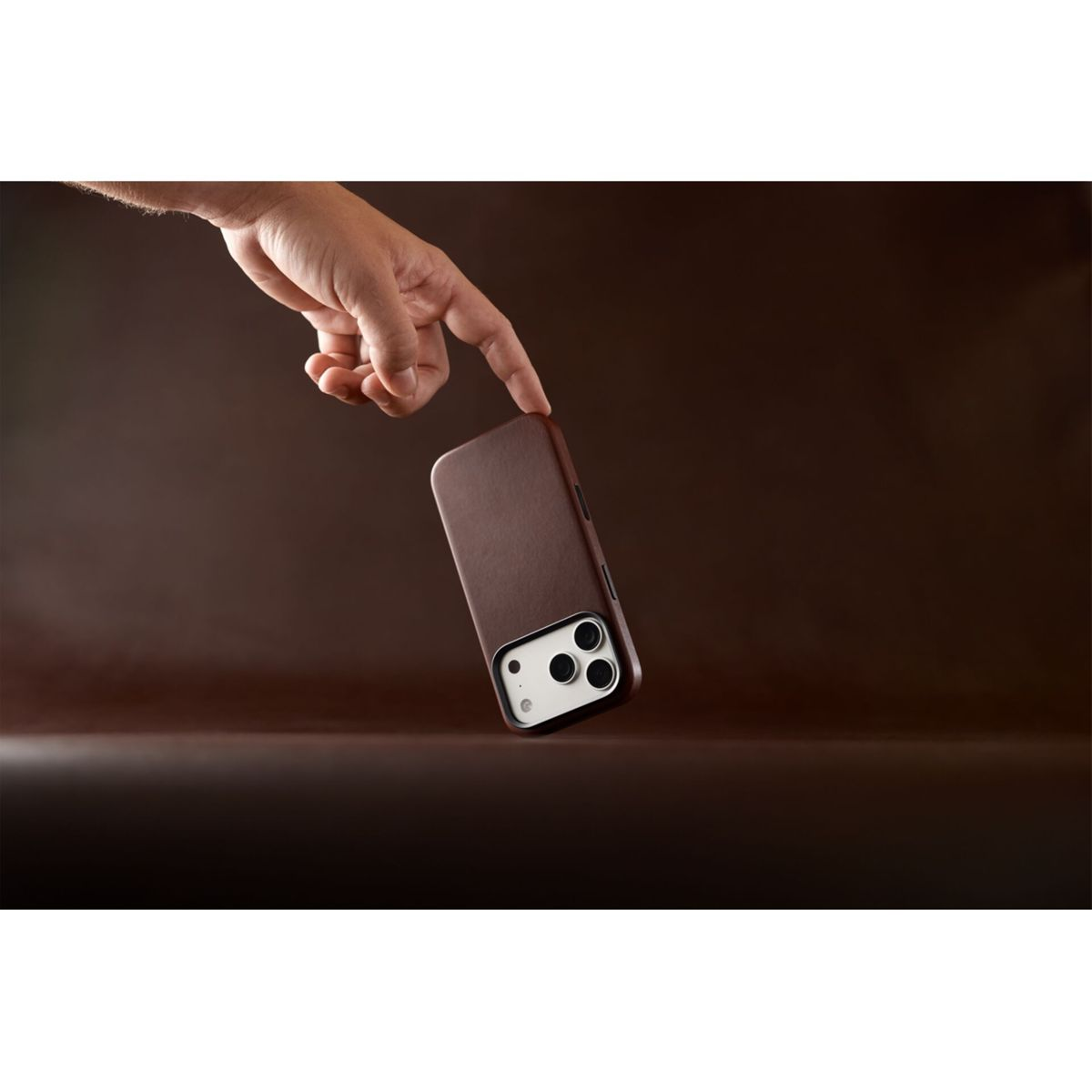 Eine Hand zeigt auf ein Smartphone in einer braunen Lederhülle vor braunem Hintergrund.