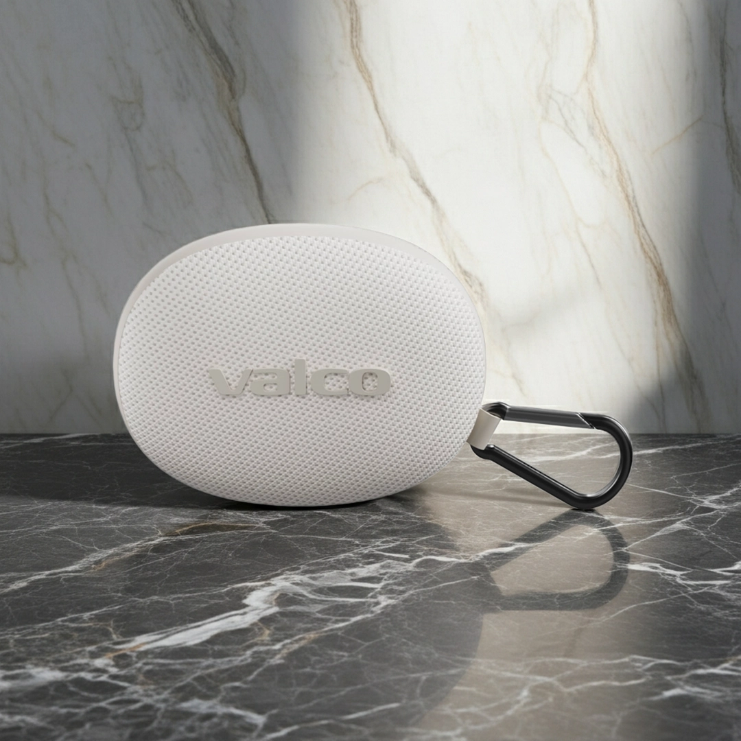 Ein weißer, ovaler Valco-Lautsprecher mit schwarzem Karabiner liegt auf dunklem Marmor vor heller Marmorwand.