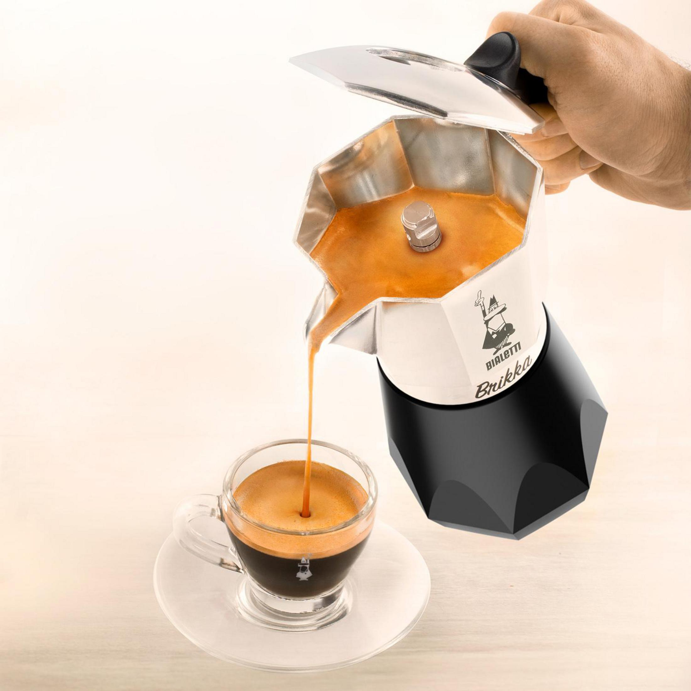 Ręka nalewa świeże espresso z kawiarki Bialetti do małej filiżanki na spodeczku.
