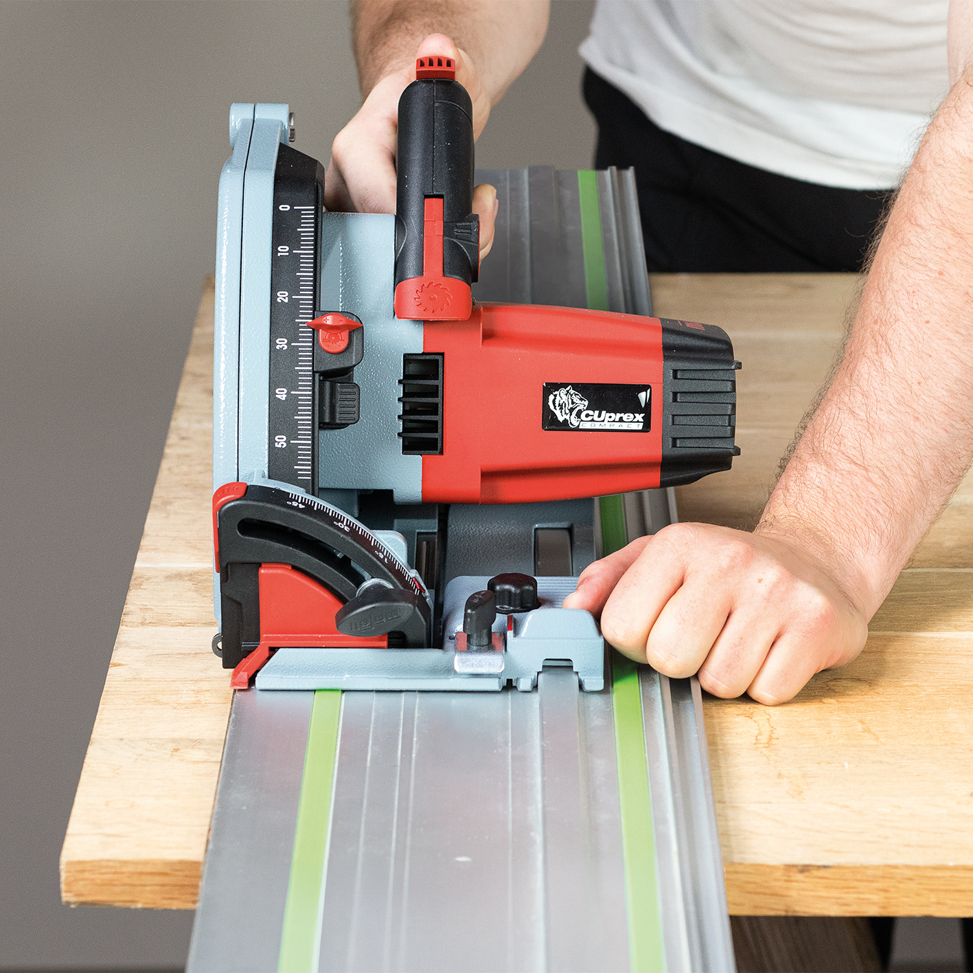 Ein Handwerker hält eine rot-graue Kreissäge auf einer Führungsschiene auf Holz.