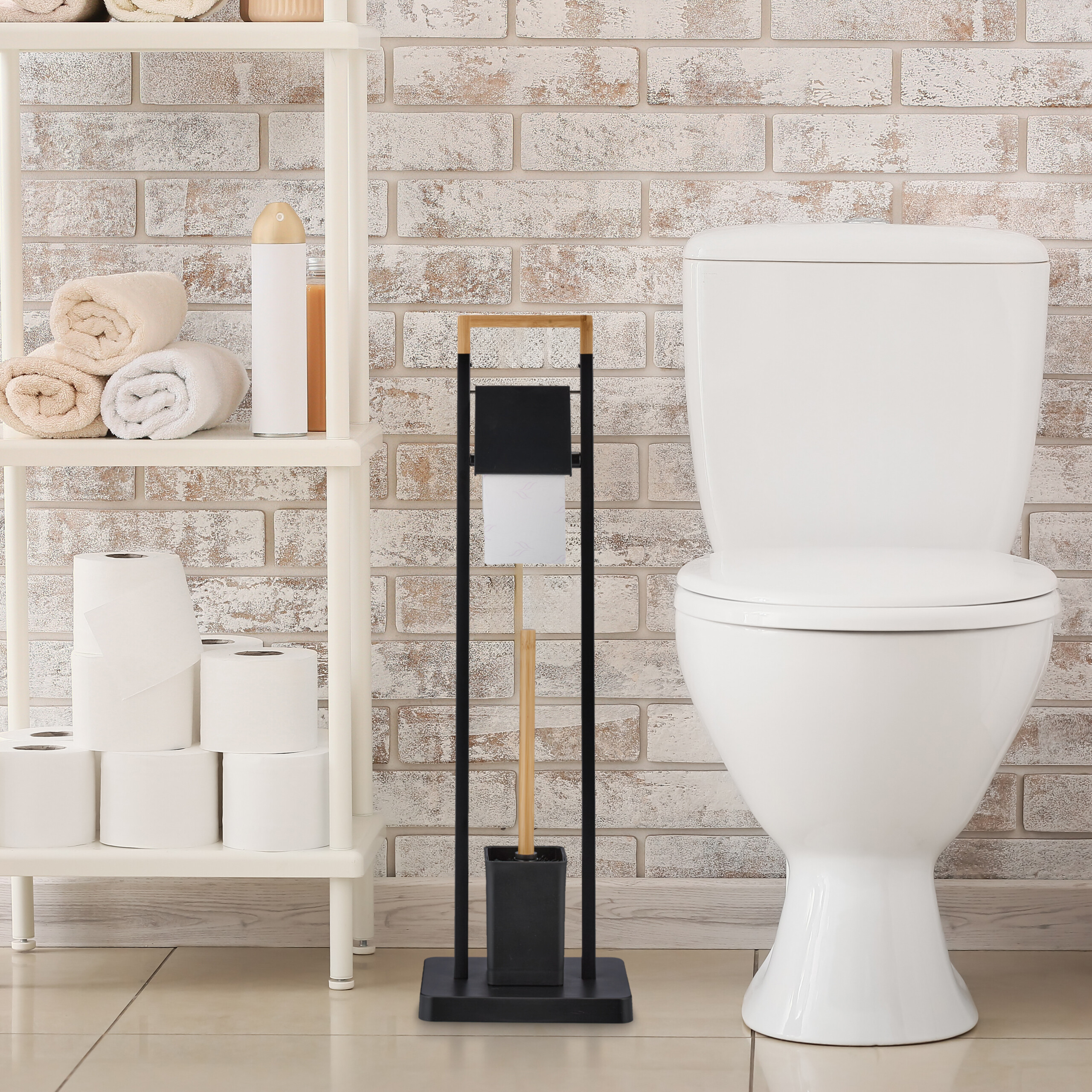 Eine weiße Toilette, ein Toilettenpapier- und Bürstenhalter aus Metall sowie ein Regal mit Handtüchern vor einer Ziegelwand.