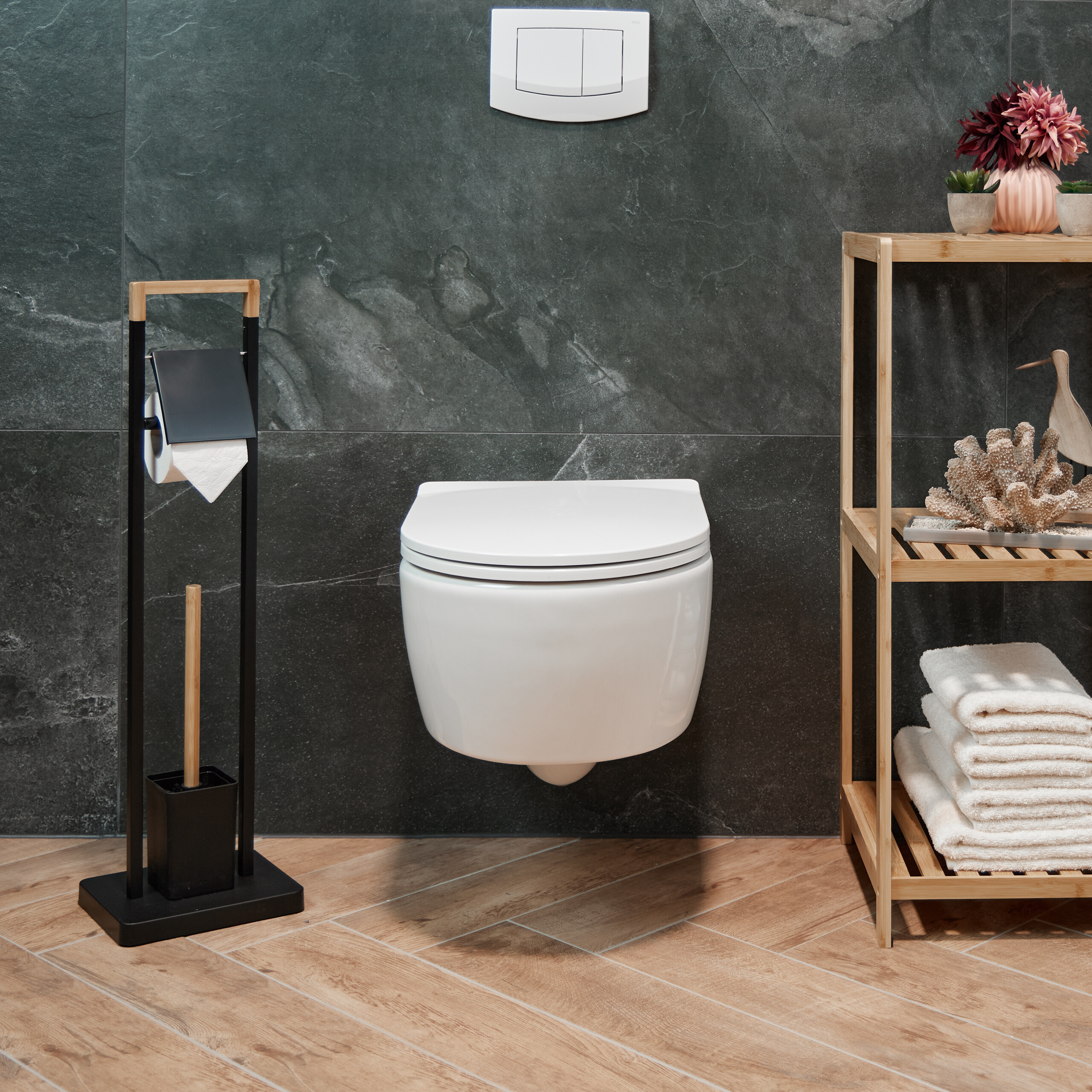 Moderne weiße Toilette vor dunkelgrauen Fliesen mit Holzboden, WC-Garnitur und Holzregal mit Handtüchern.