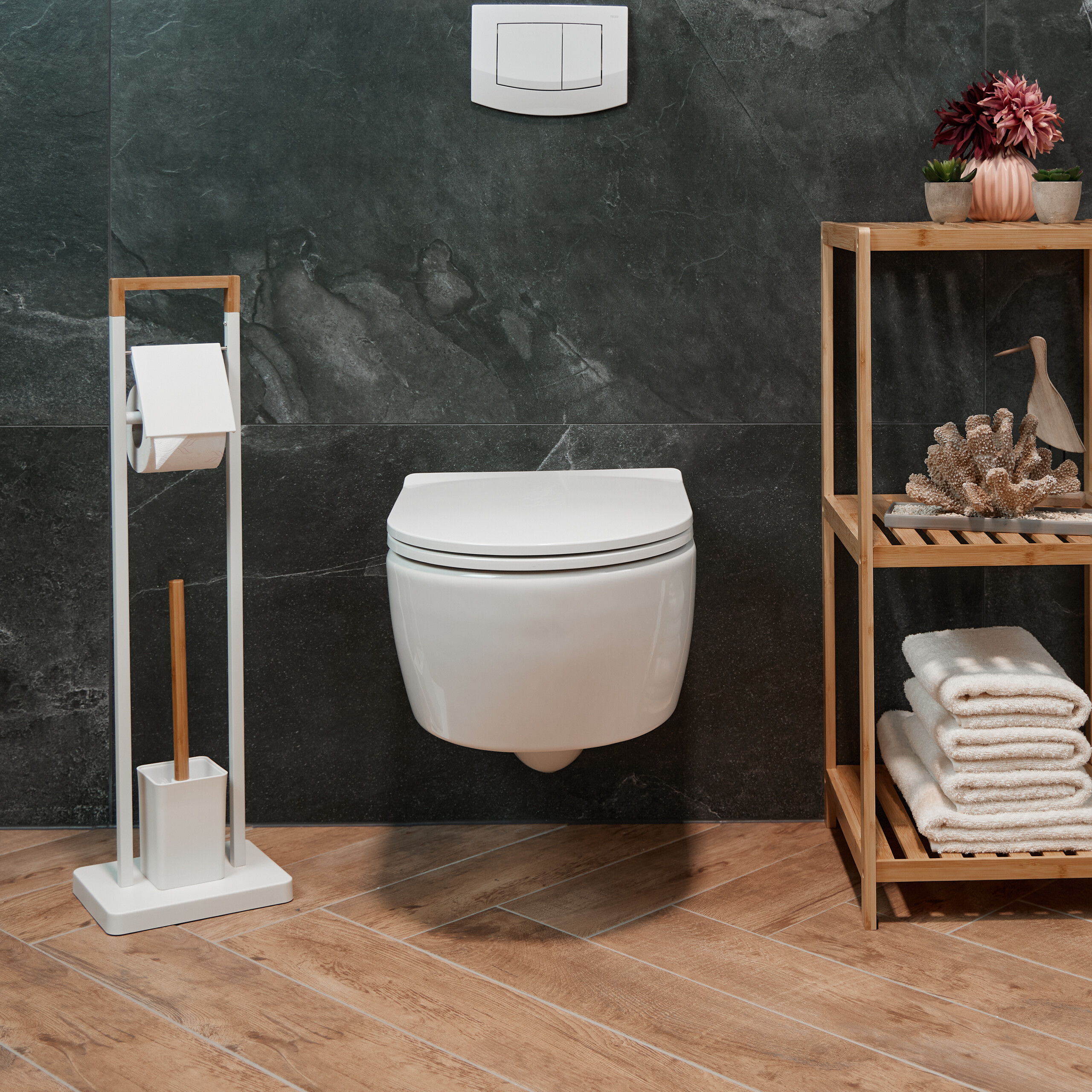 Ein modernes weißes Wand-WC vor dunklen Steinplatten, mit Holzregal, Toilettenpapierhalter und Holzfußboden.