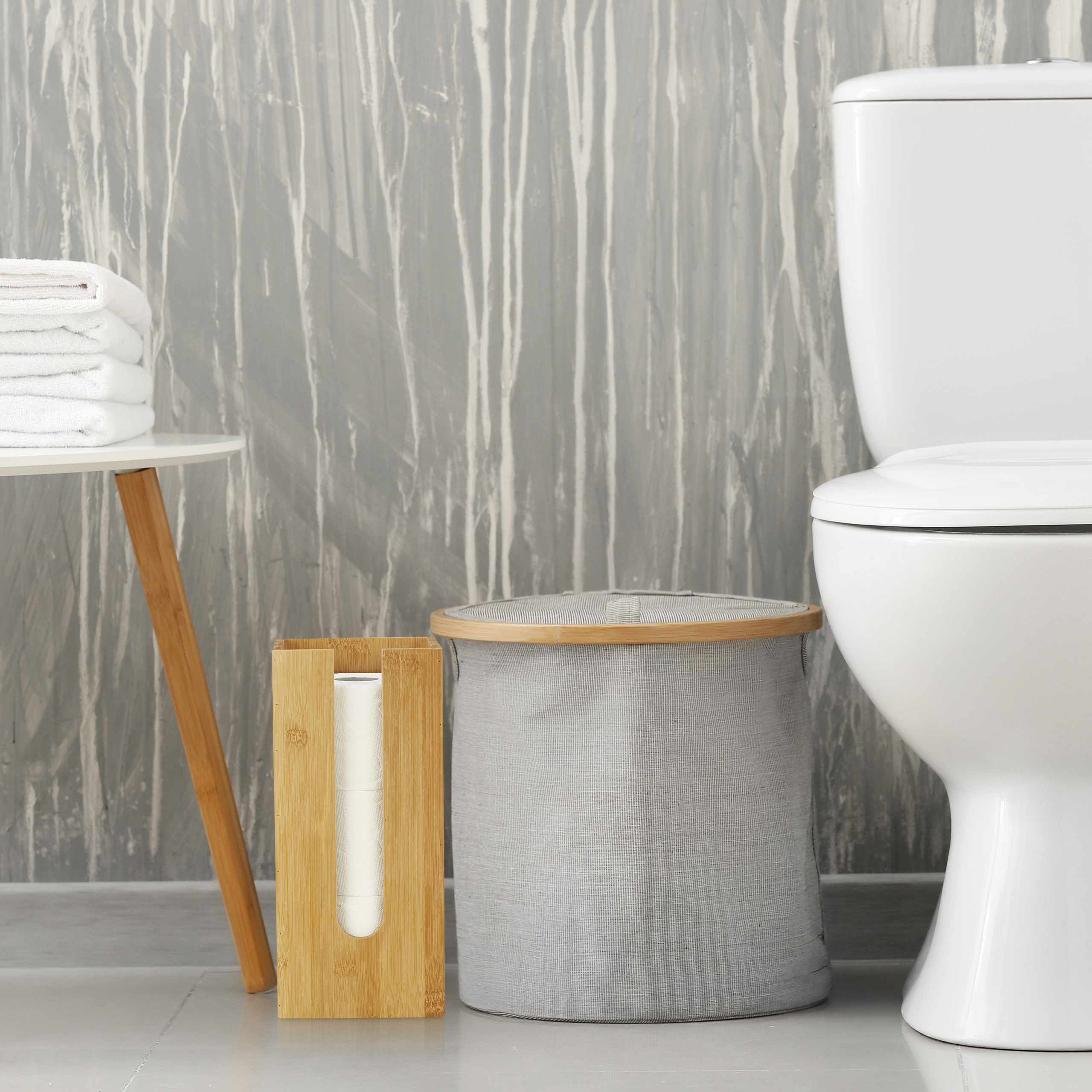 Moderne Badezimmerreinrichtung mit Toilette, Wäschekorb, Holztuchhalter und Handtüchern vor grauer Wand.