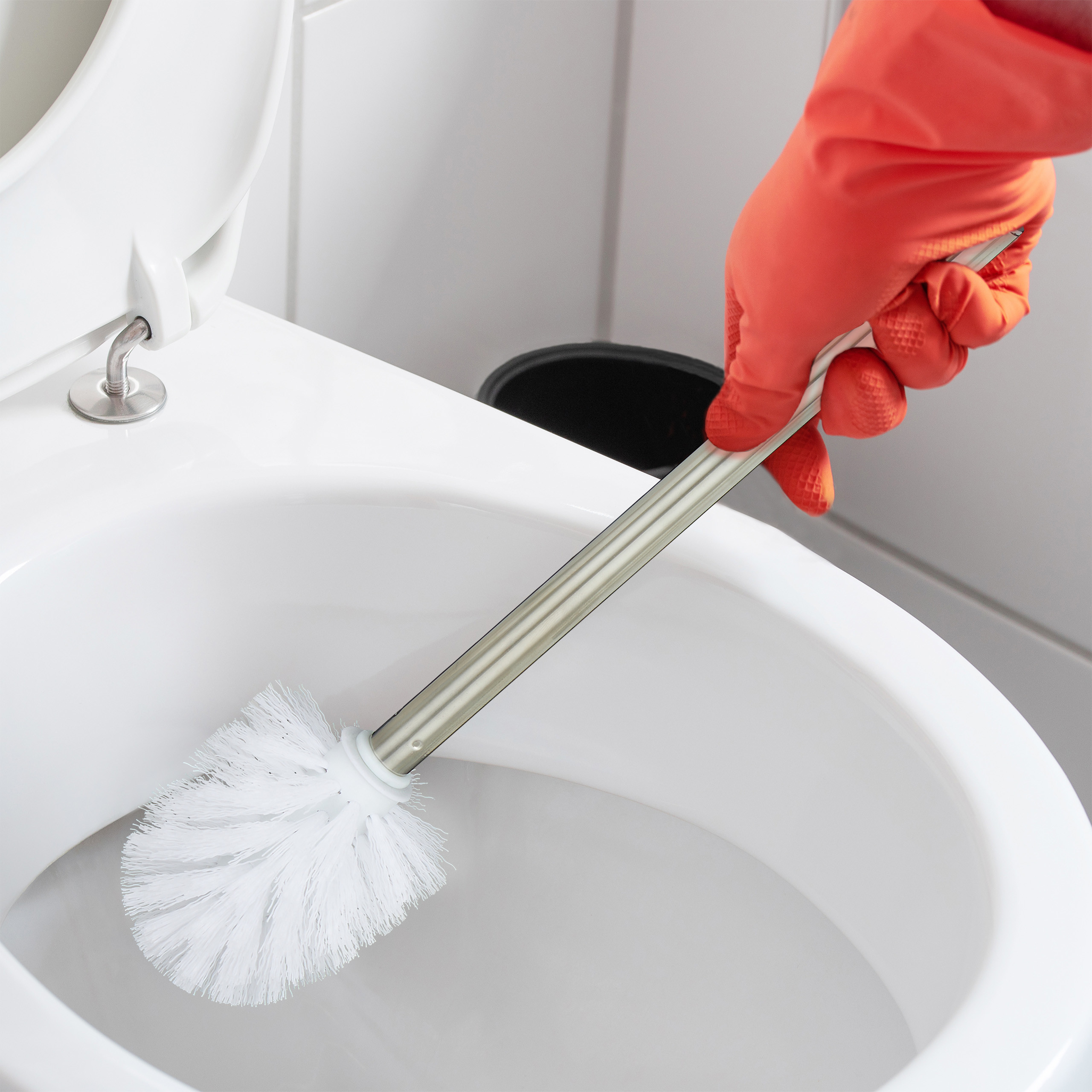 Eine Hand in einem orangefarbenen Handschuh putzt eine weiße Toilette mit einer Bürste.