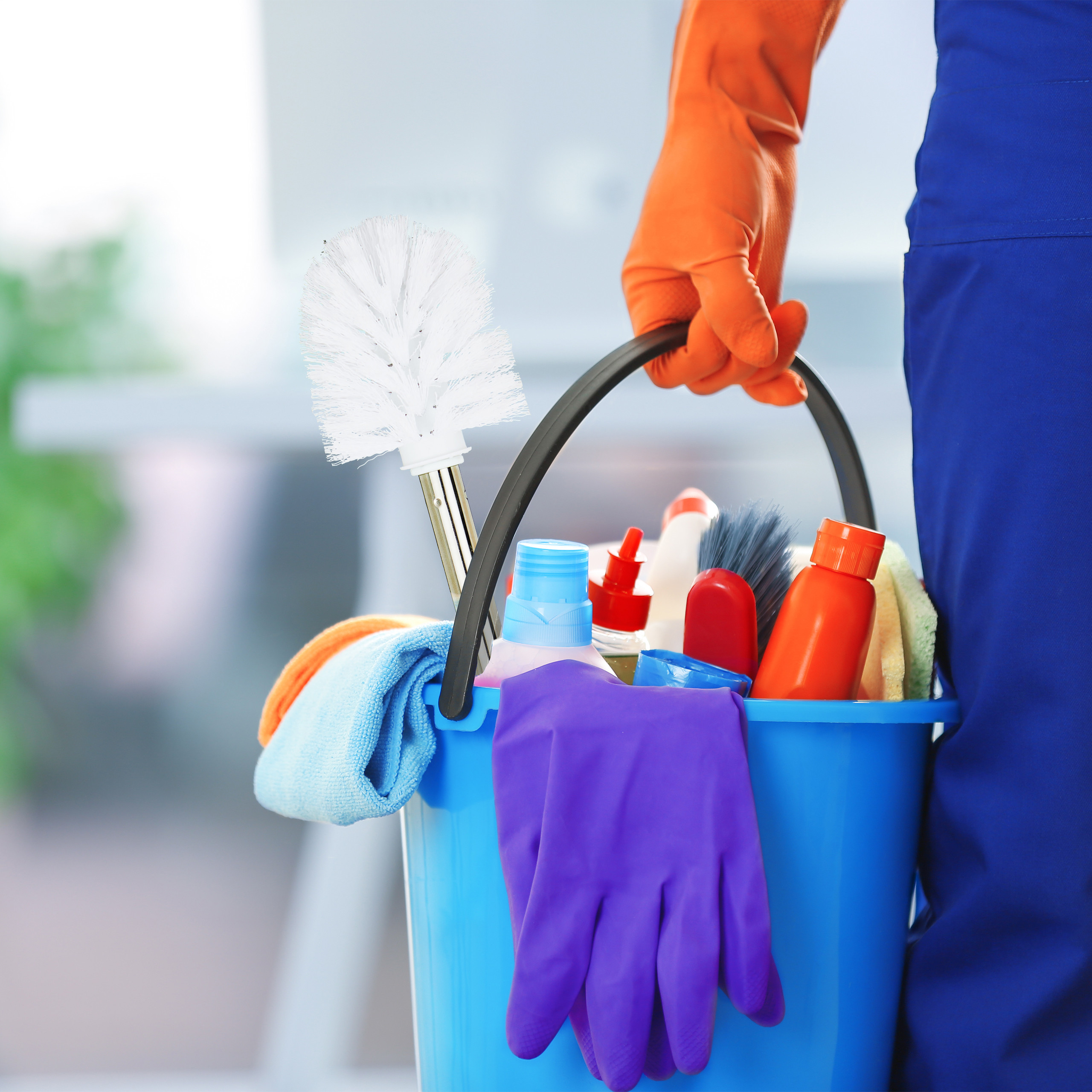Eine Person in blauer Kleidung hält einen blauen Putzeimer mit Reinigungsutensilien, Bürsten und Tüchern.