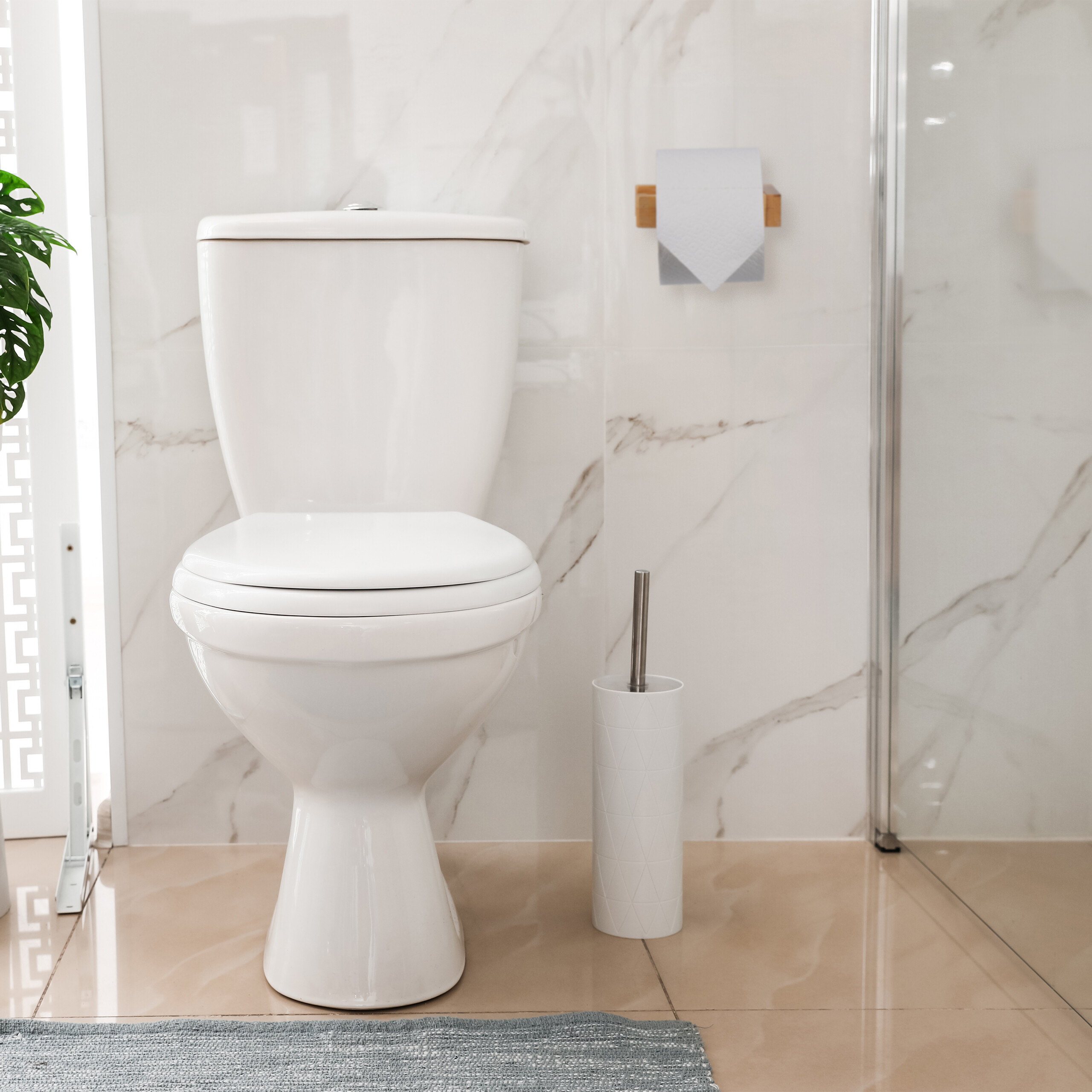 Eine weiße Toilette steht in einem Badezimmer mit Marmorwänden, einer Klobürste daneben und Papierrollenhalter an der Wand.