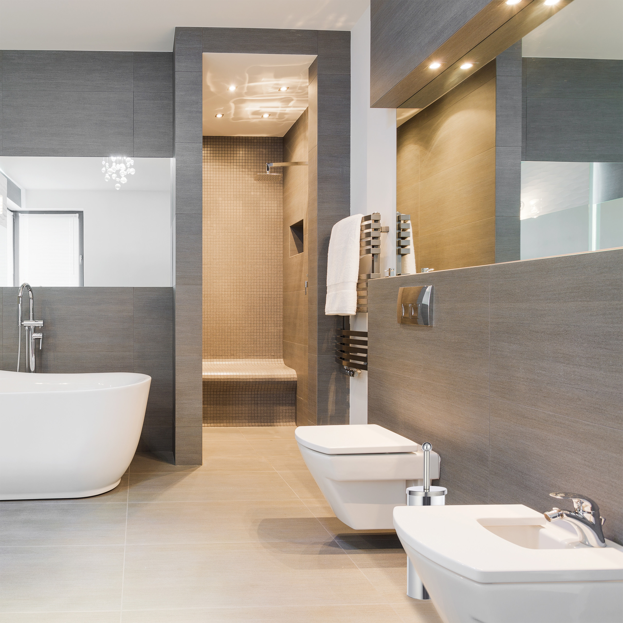 Luxuriöses, modernes Badezimmer mit grauen Fliesen, freistehender Badewanne, Dusche und Toilette.