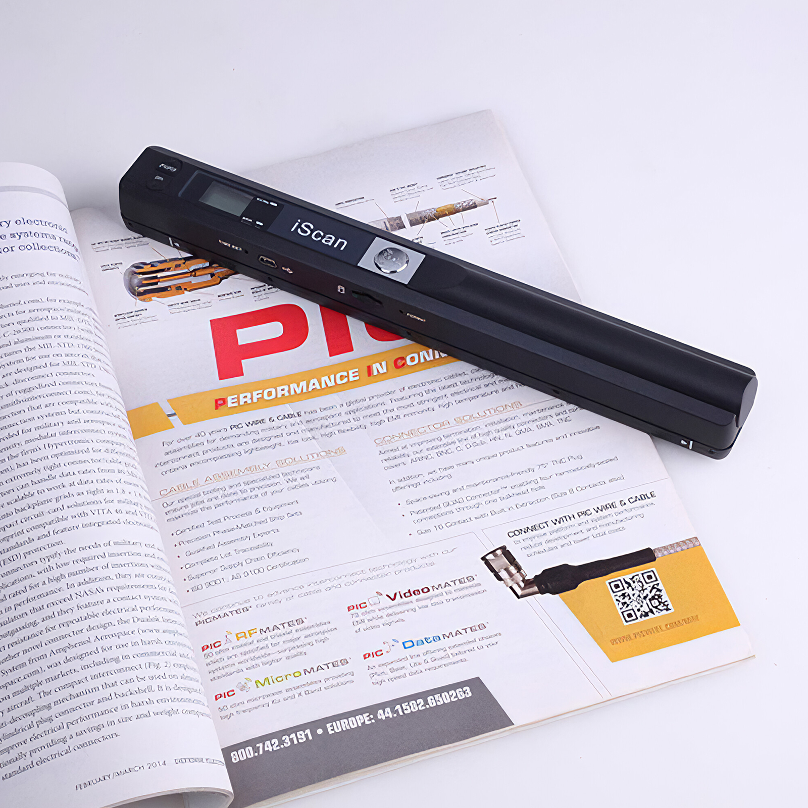 Ein schwarzer tragbarer Handscanner liegt aufgeschlagen auf einer Zeitschrift mit Text und Grafiken.